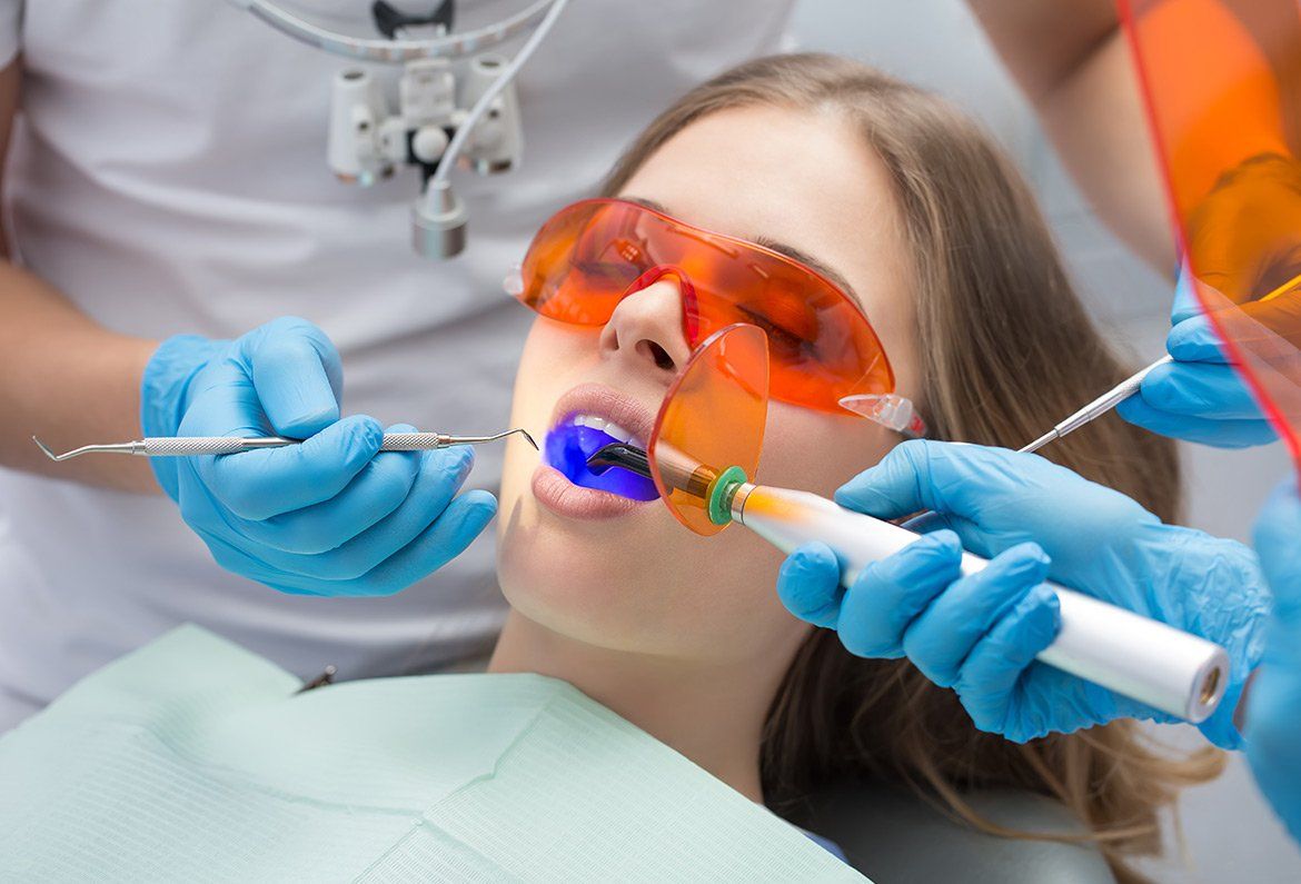 Dentist using curing light on patient's teeth during a procedure, protective eyewear on.