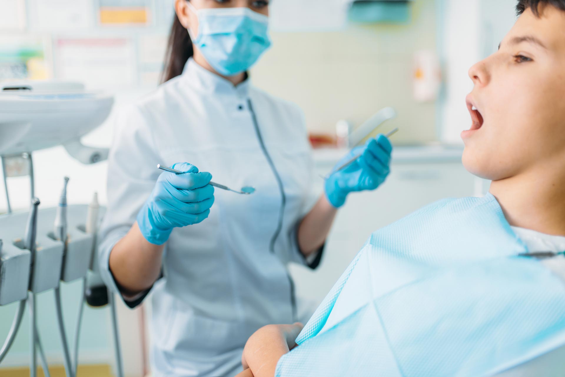 Dentist examining a patient's mouth with tools in a dental office. The patient is sitting in a chair.