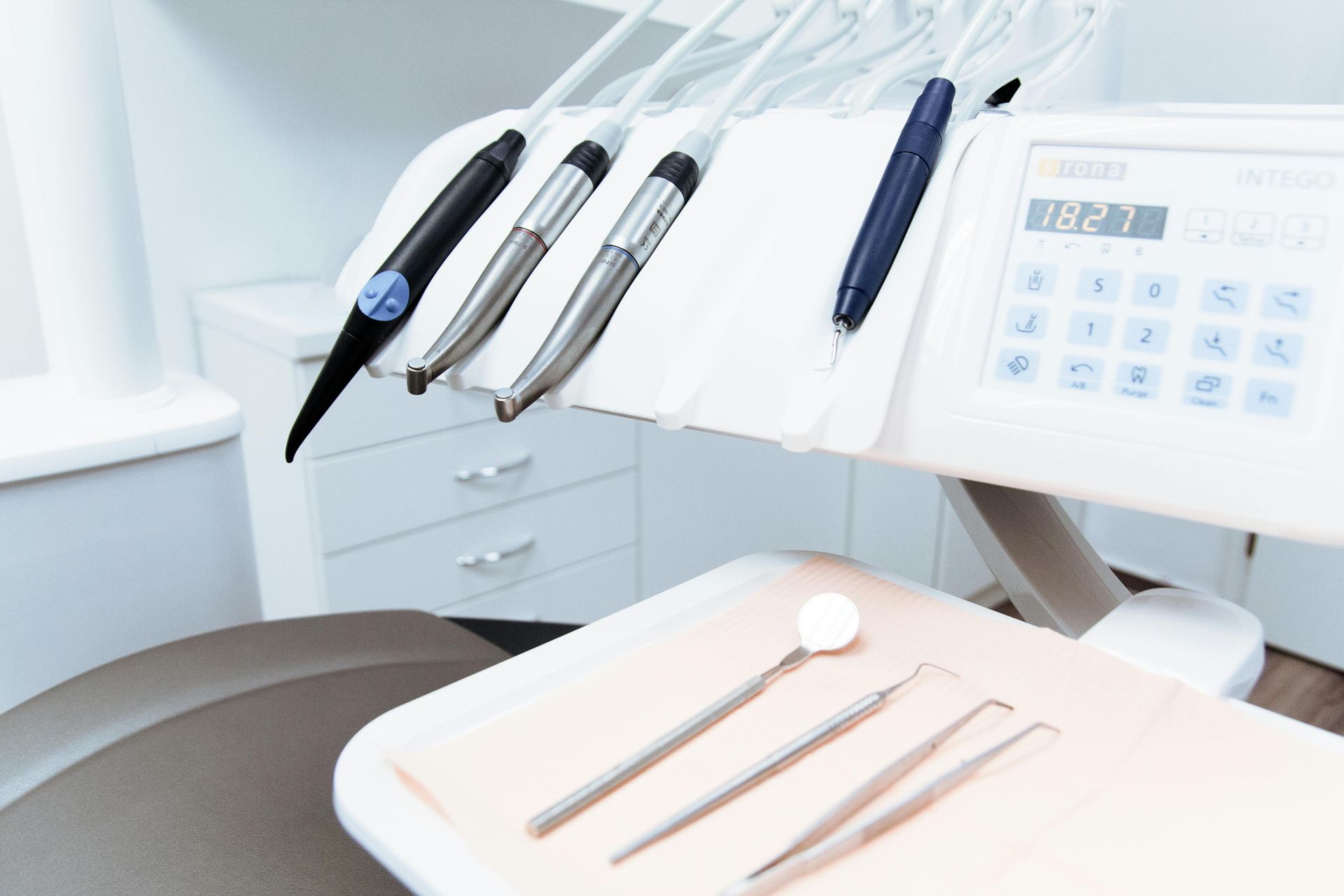 Dental tools on a tray in a dentist's office, with dental equipment in the background.