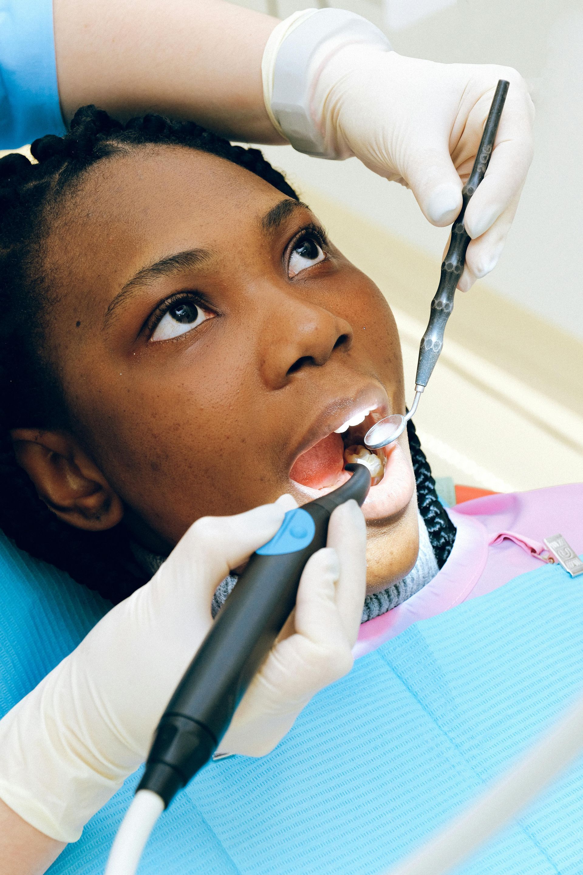 Dentist performing dental work on a patient. Patient's mouth open, tools in use. Hands in gloves.