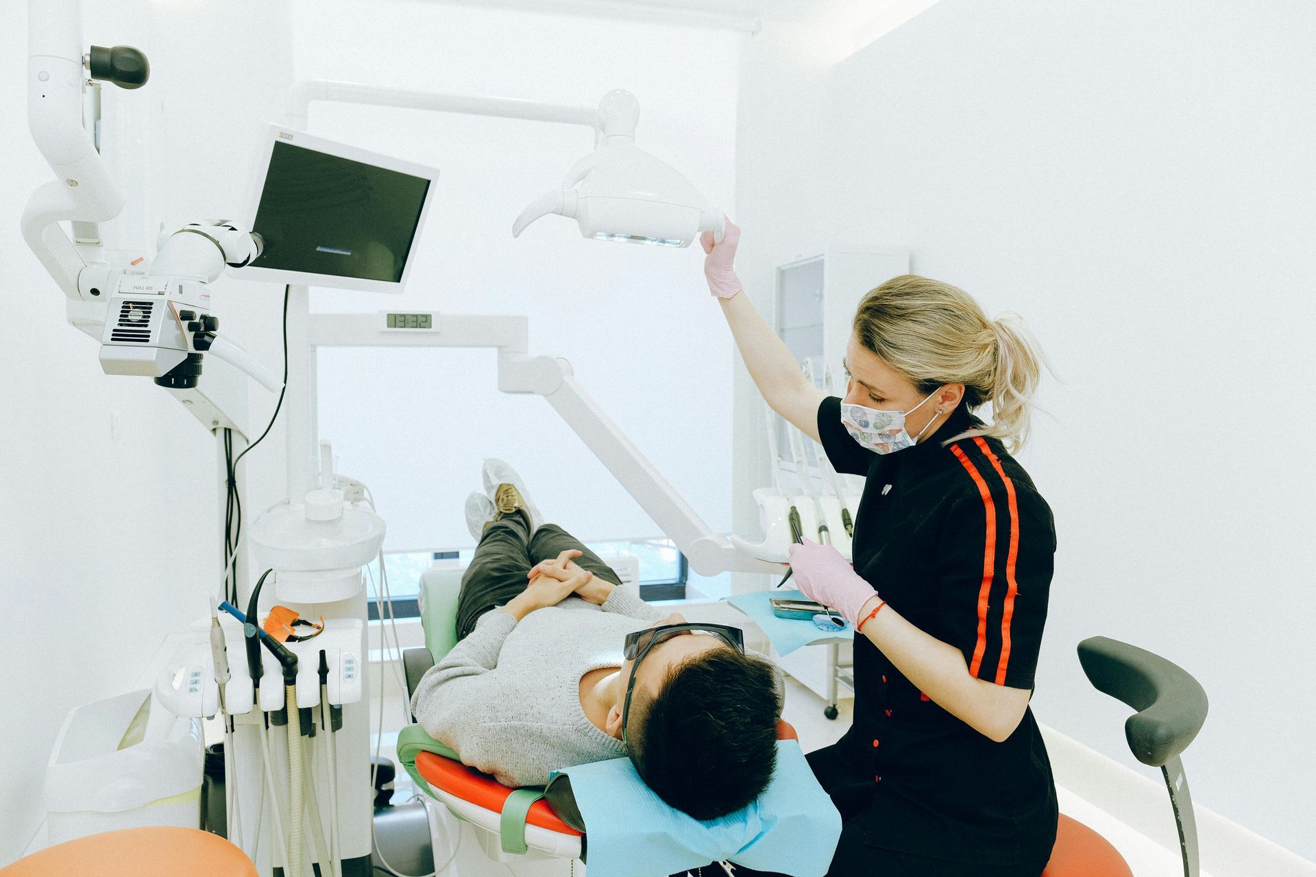 Dentist adjusting light over a patient in a dental chair; bright, white office setting.