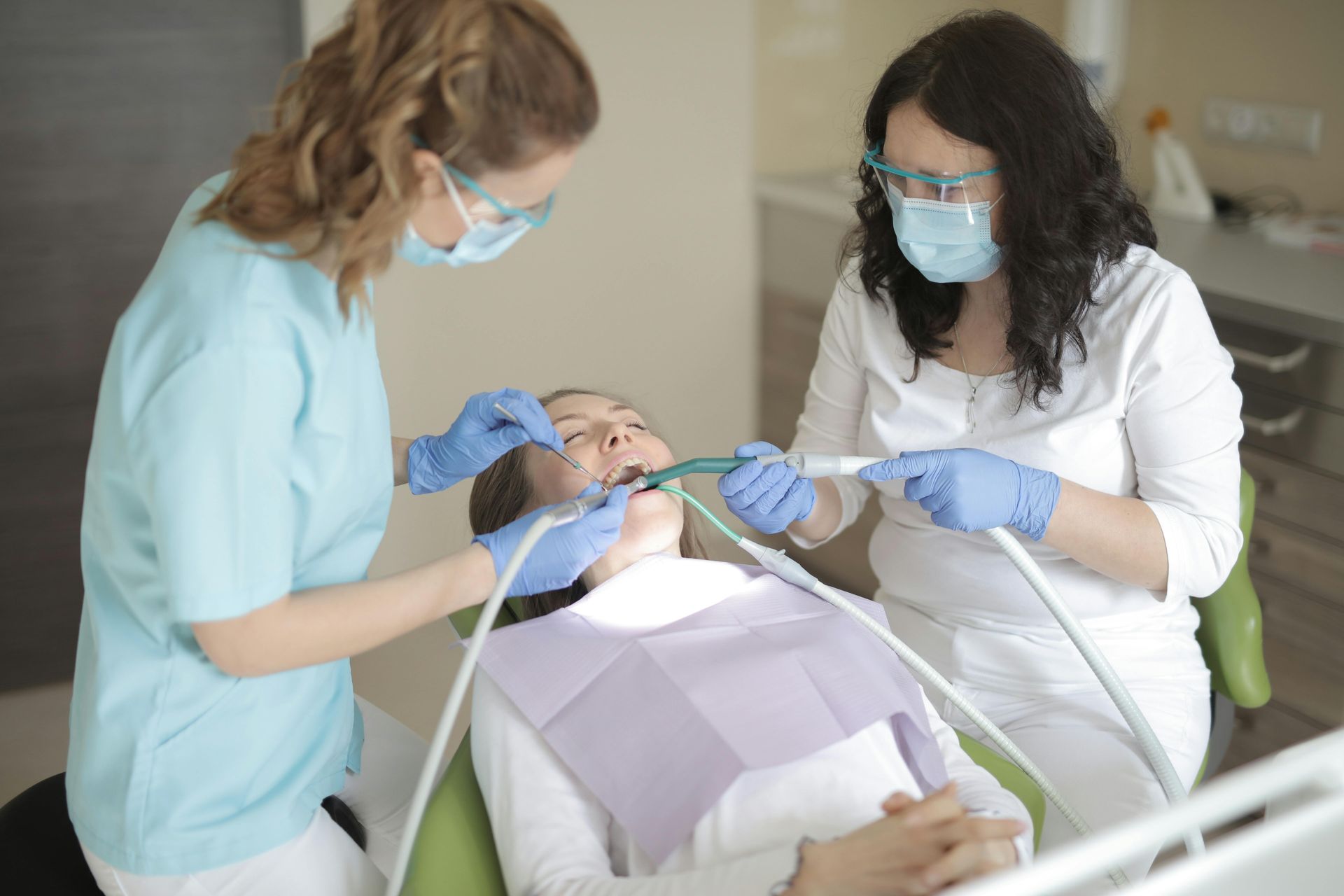 A person receiving dental treatment from two dental professionals, all wearing protective gear.