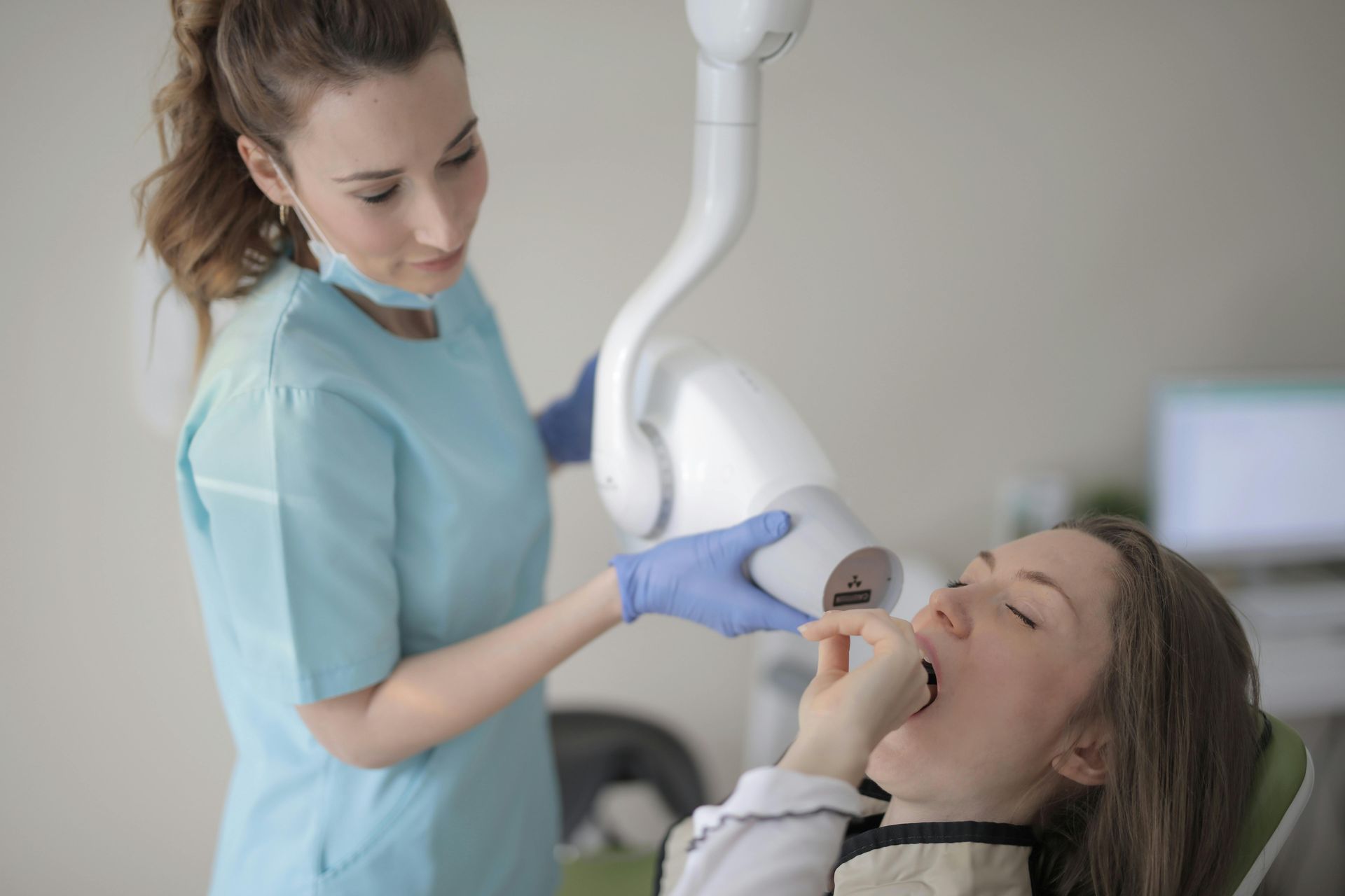 Dentist taking X-ray of a patient's teeth. Dentist is wearing gloves and a light blue scrub top.