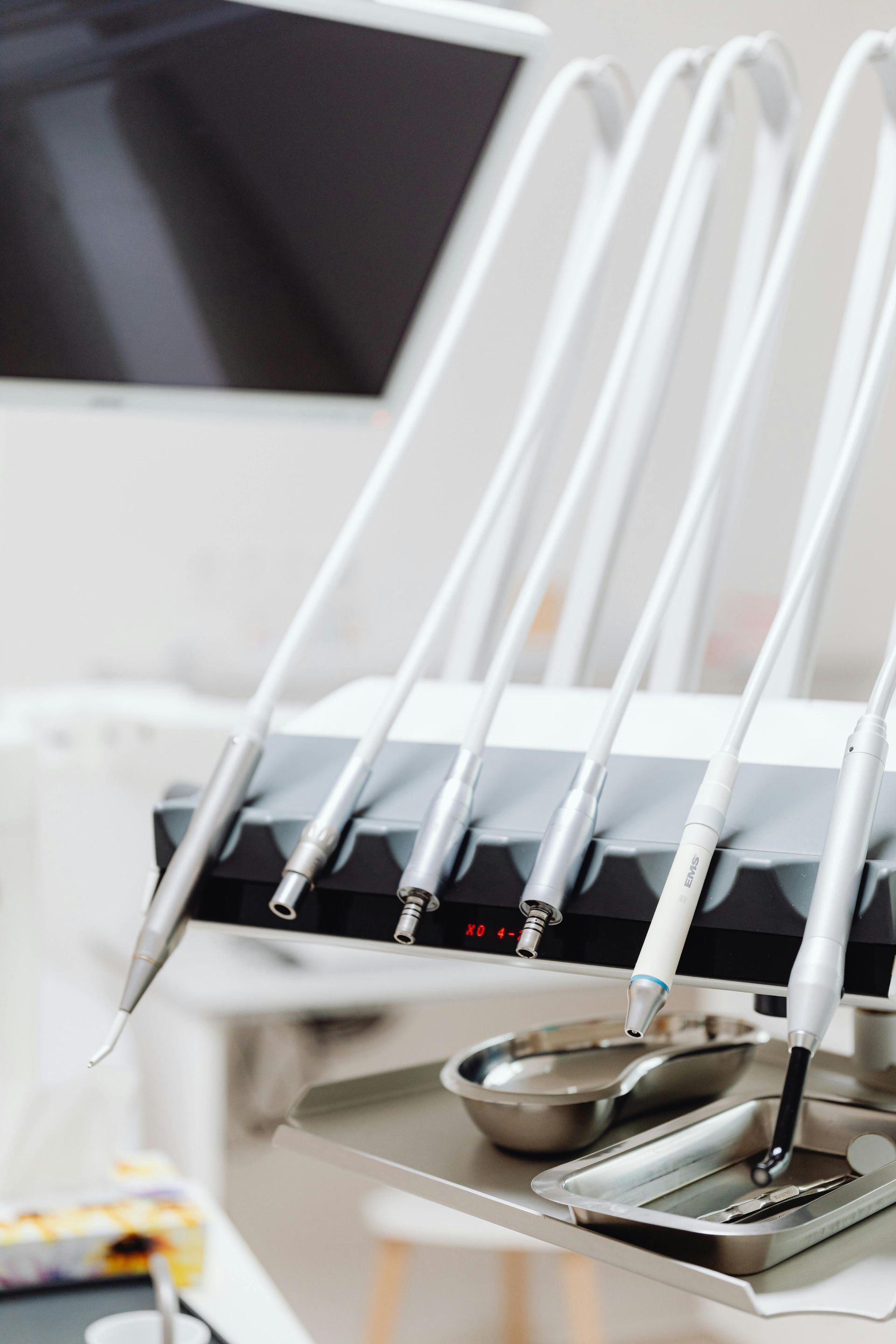 Dental tools mounted on a workstation in a dentist's office, with a tray of instruments in the foreground.