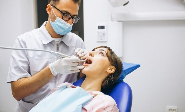 Dentist using a handpiece on a patient's teeth in a dental office. The patient has mouth open.