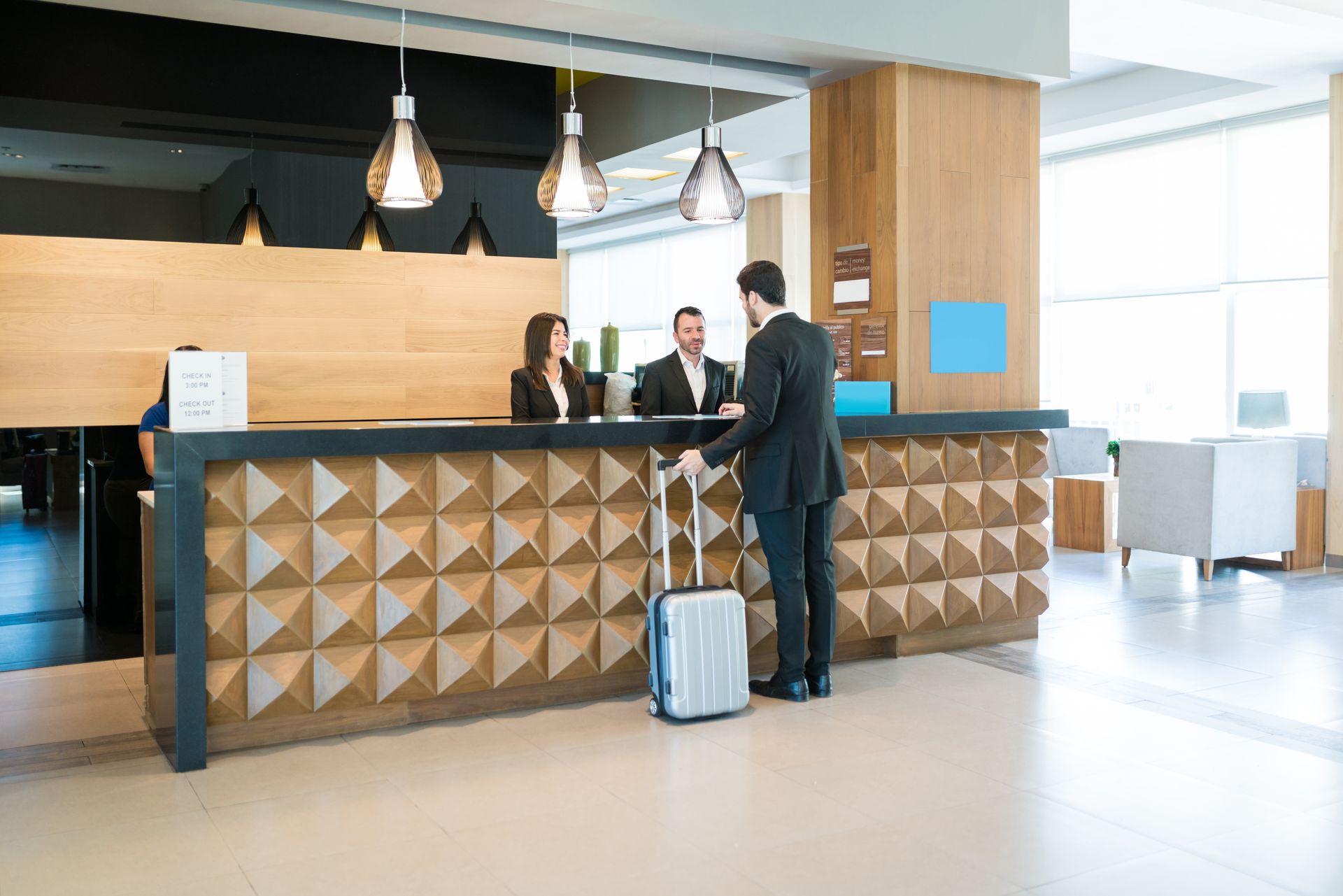 A man with a suitcase is standing at a hotel counter