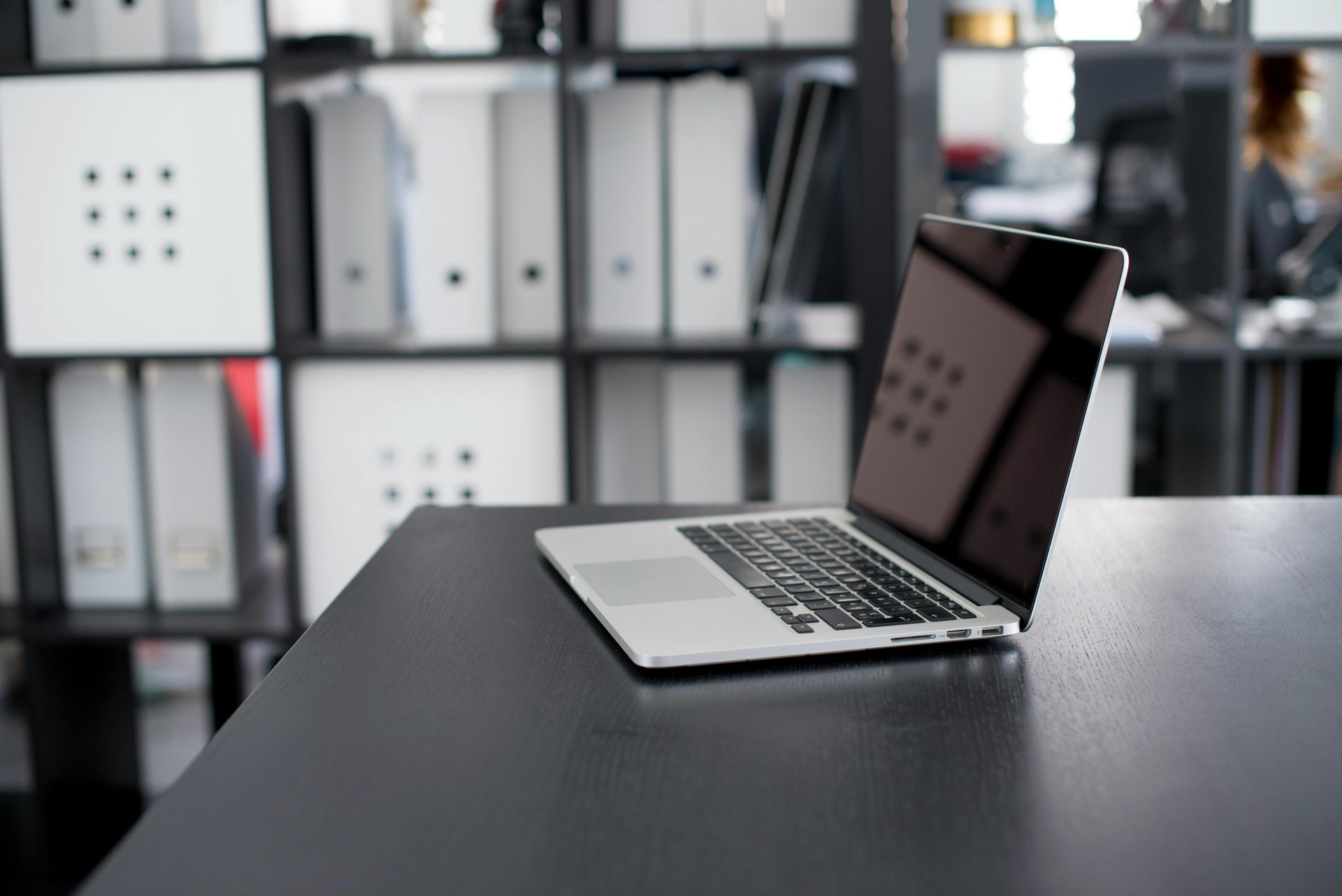 A laptop is open on a desk with binders in the background