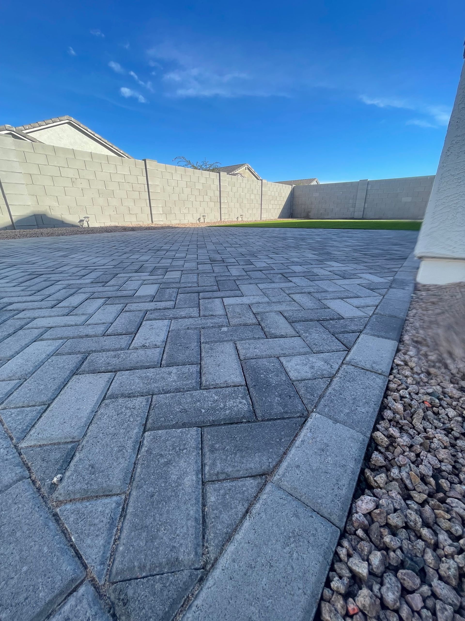 A brick driveway with a fence in the background and a blue sky in the background.