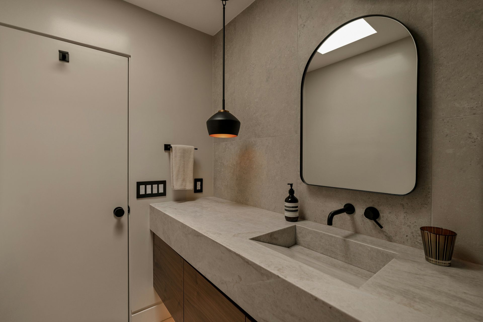 Modern bathroom with a concrete sink, arched mirror, and pendant light.