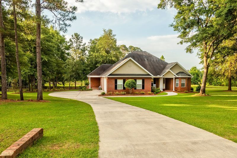 A large brick house with a long driveway leading to it surrounded by trees.