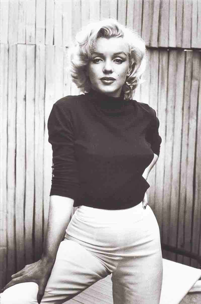 Marilyn Monroe wearing a black turtleneck and white pants.