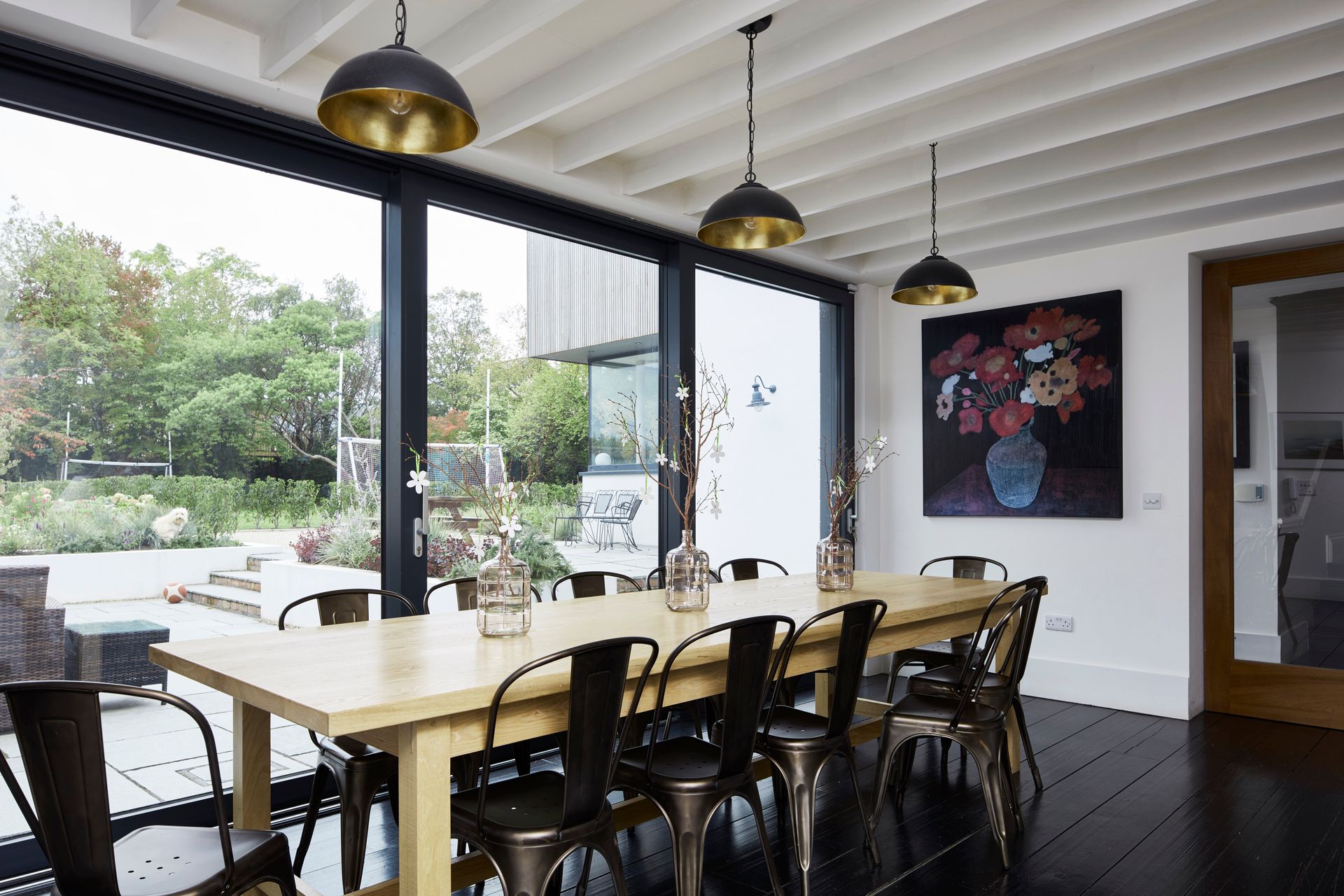 A dining room with a long table and chairs and a painting on the wall.