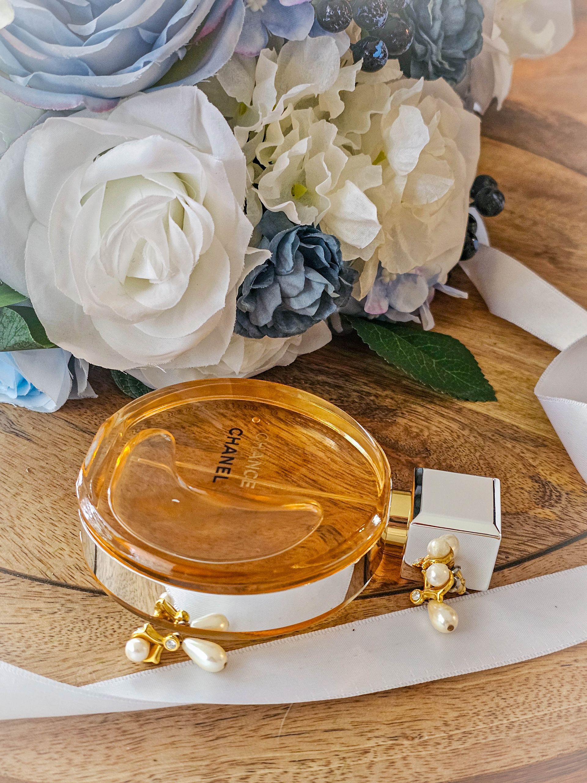 Amber Glass Cosmetic Jar with White and Blue Flowers and Pearl Hairpins on A Wooden Surface — Craig Stevens Photography in Pearl Beach, NSW