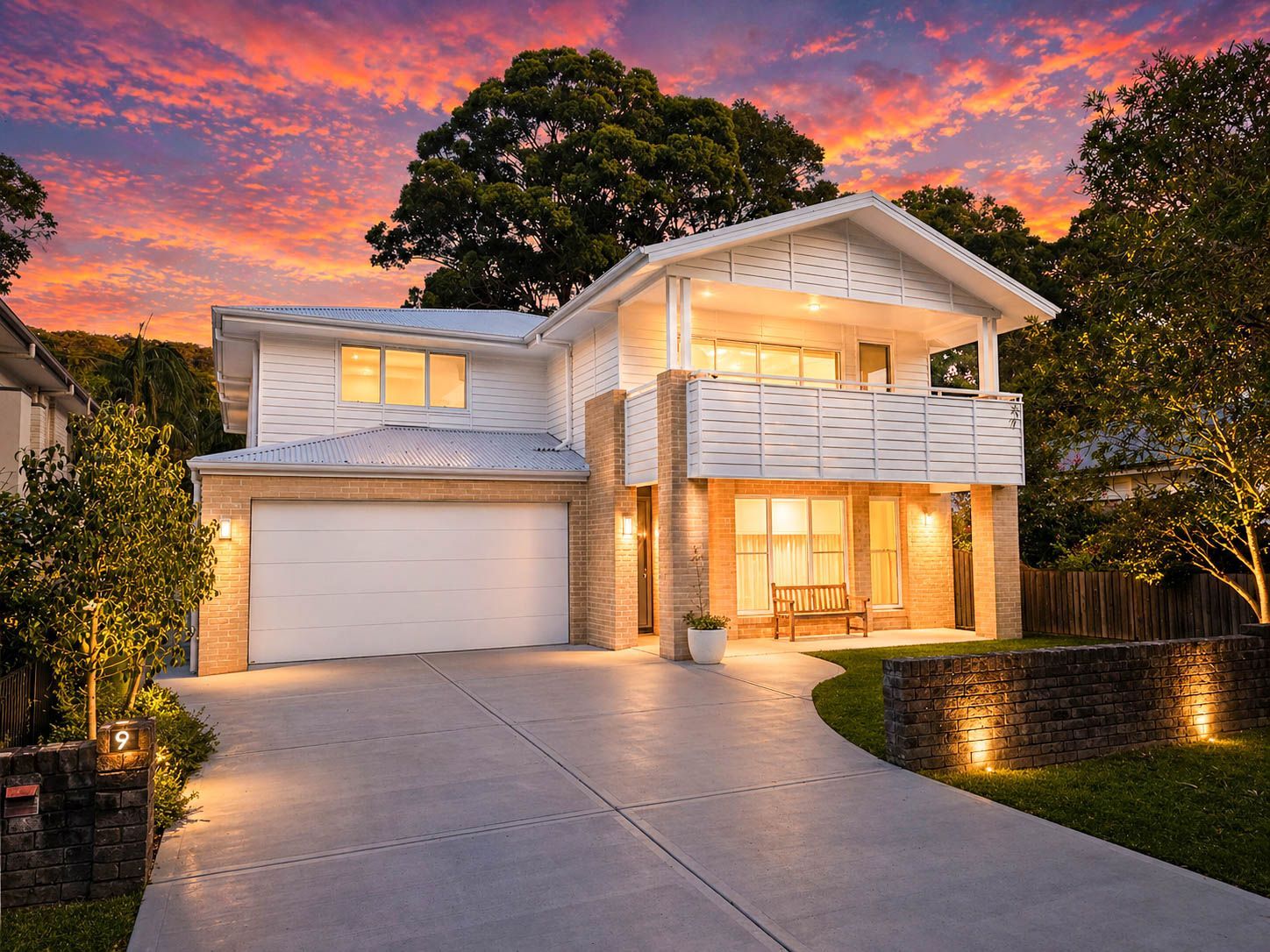 Modern two-story house with lit windows and garage at sunset under a vivid orange sky - Craig Stevens Photography in Pearl Beach, NSW
