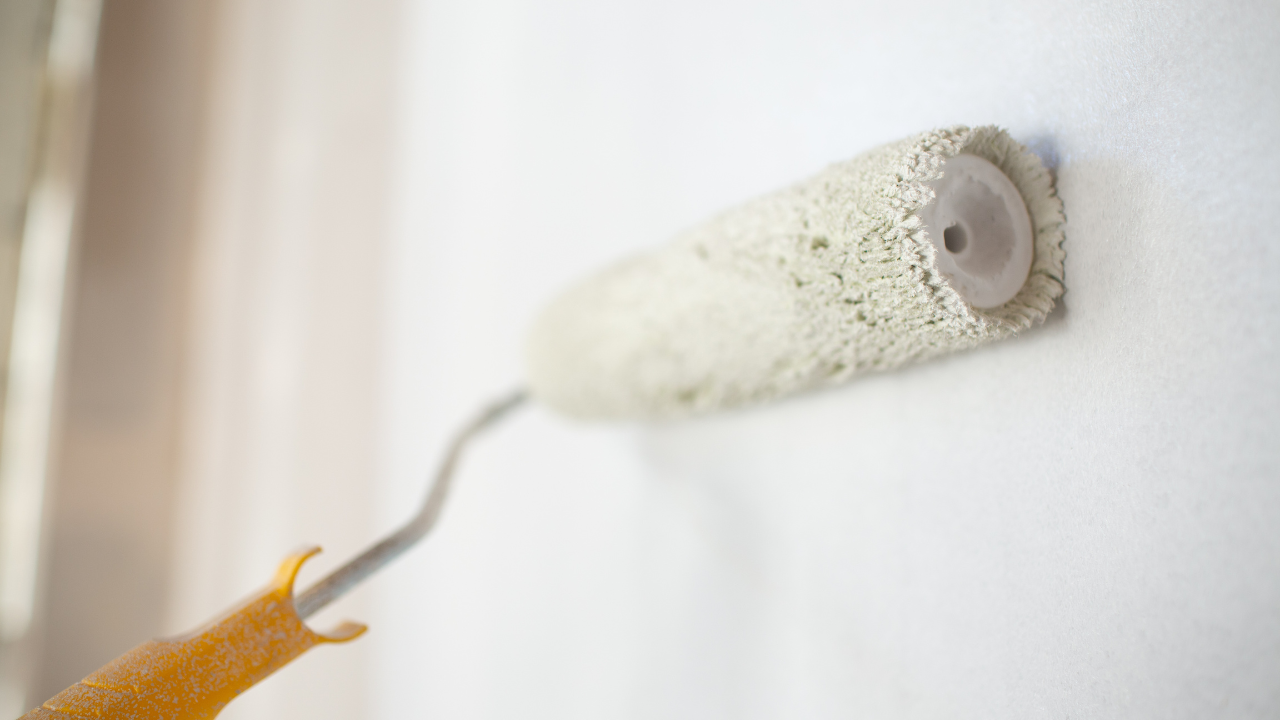 Paint roller applying white paint to a wall.
