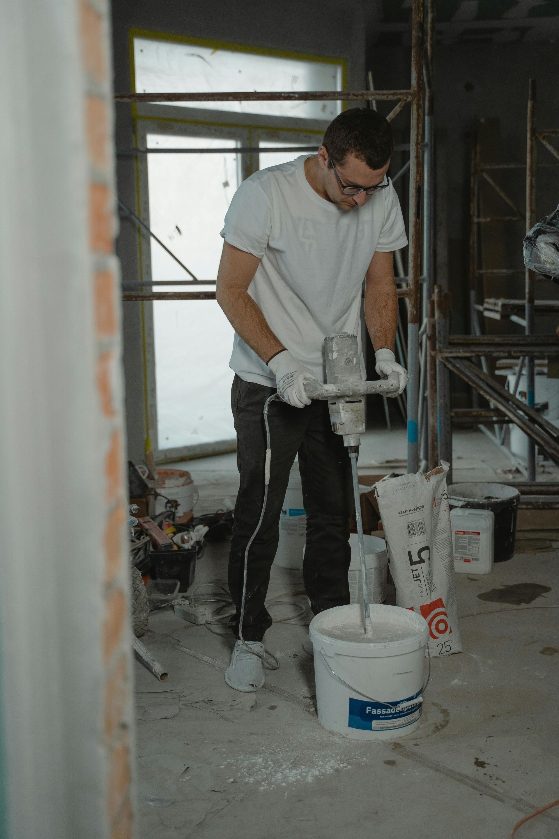 Man mixing plaster in a bucket with a power mixer, construction setting.