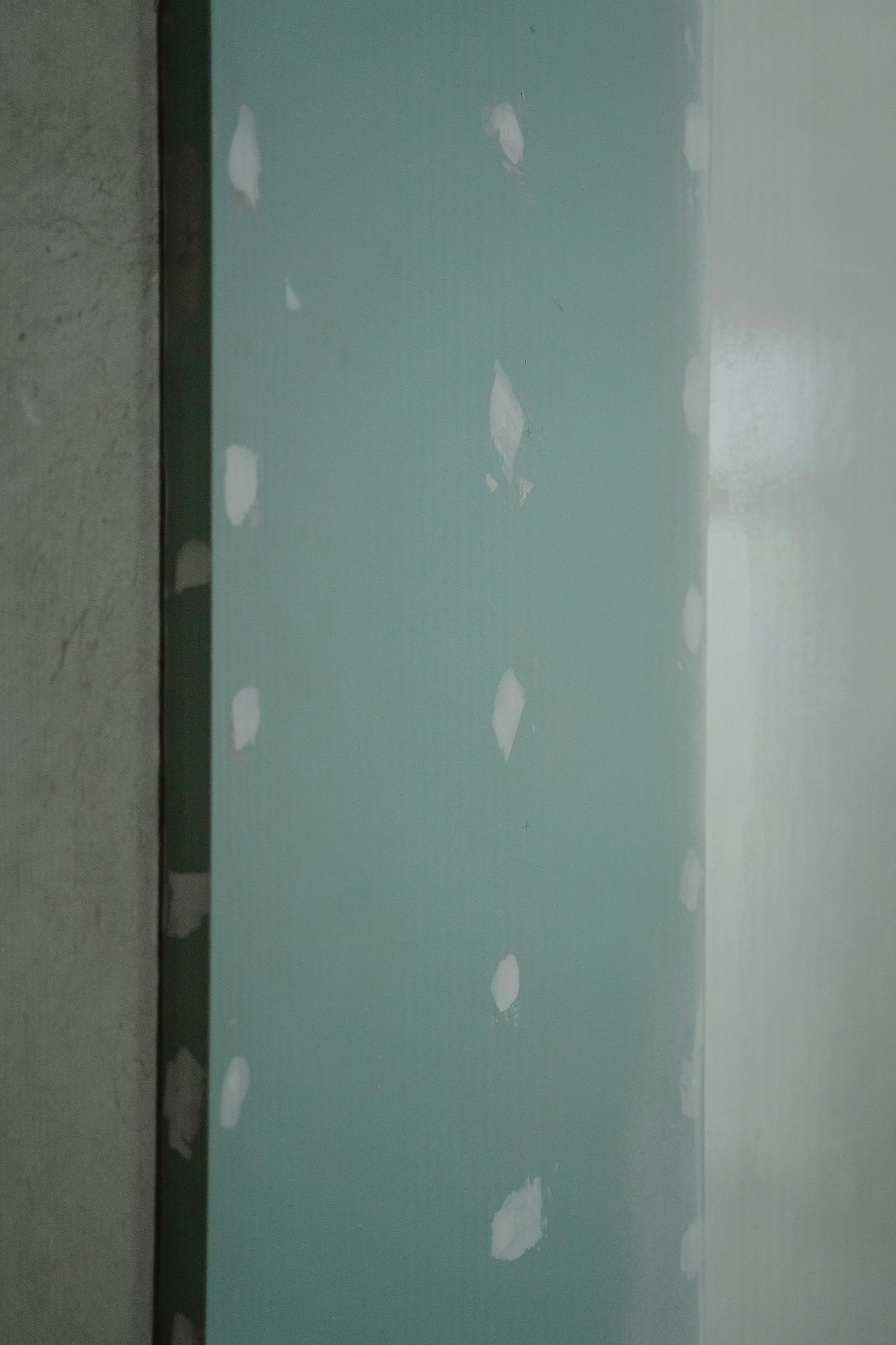 Green painted wall with several white patched spots.