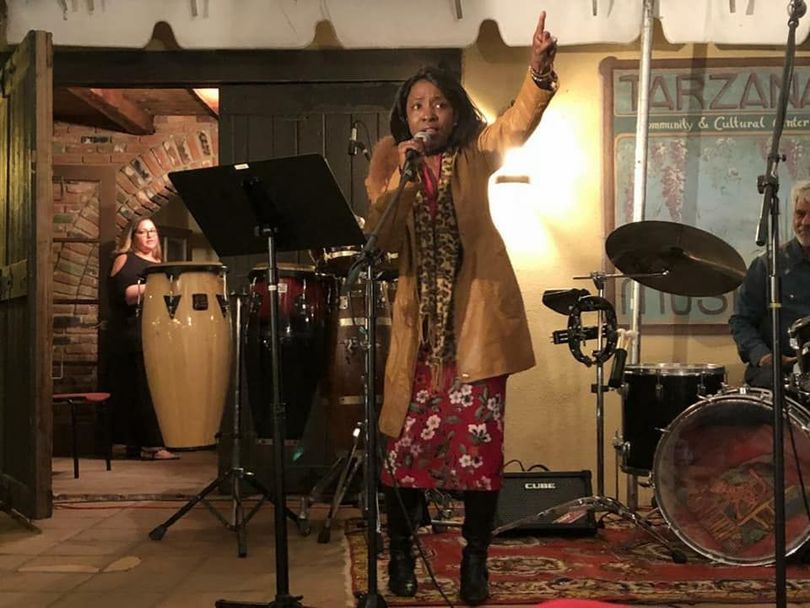 A woman is singing into a microphone on a stage in front of a drum set.