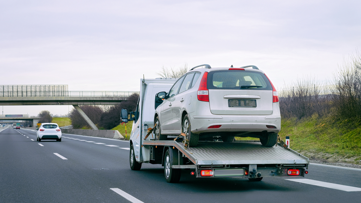 A tow truck is towing a white car on a highway.