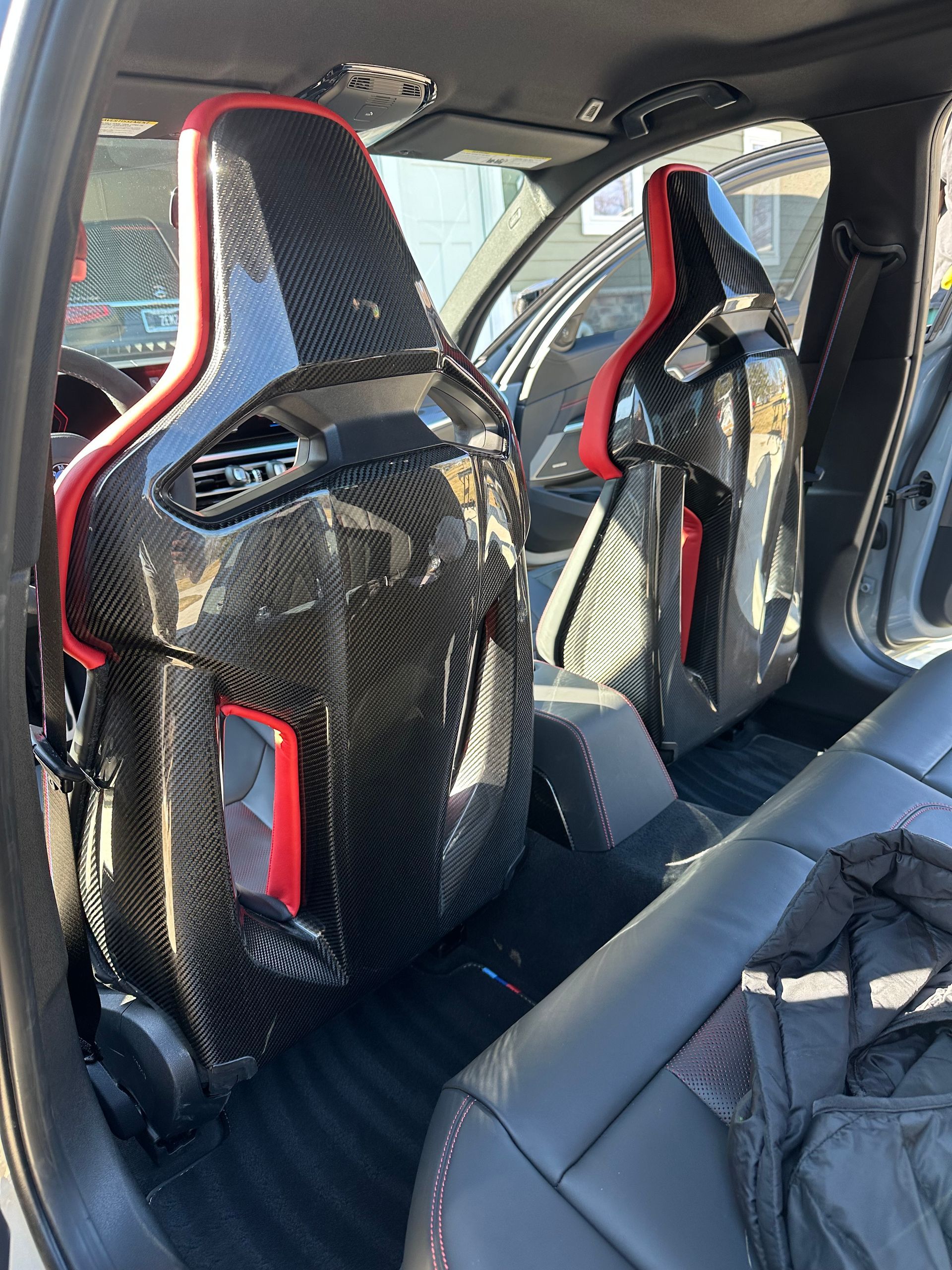 Car interior with two carbon-fiber racing seats with red accents and black leather upholstery.