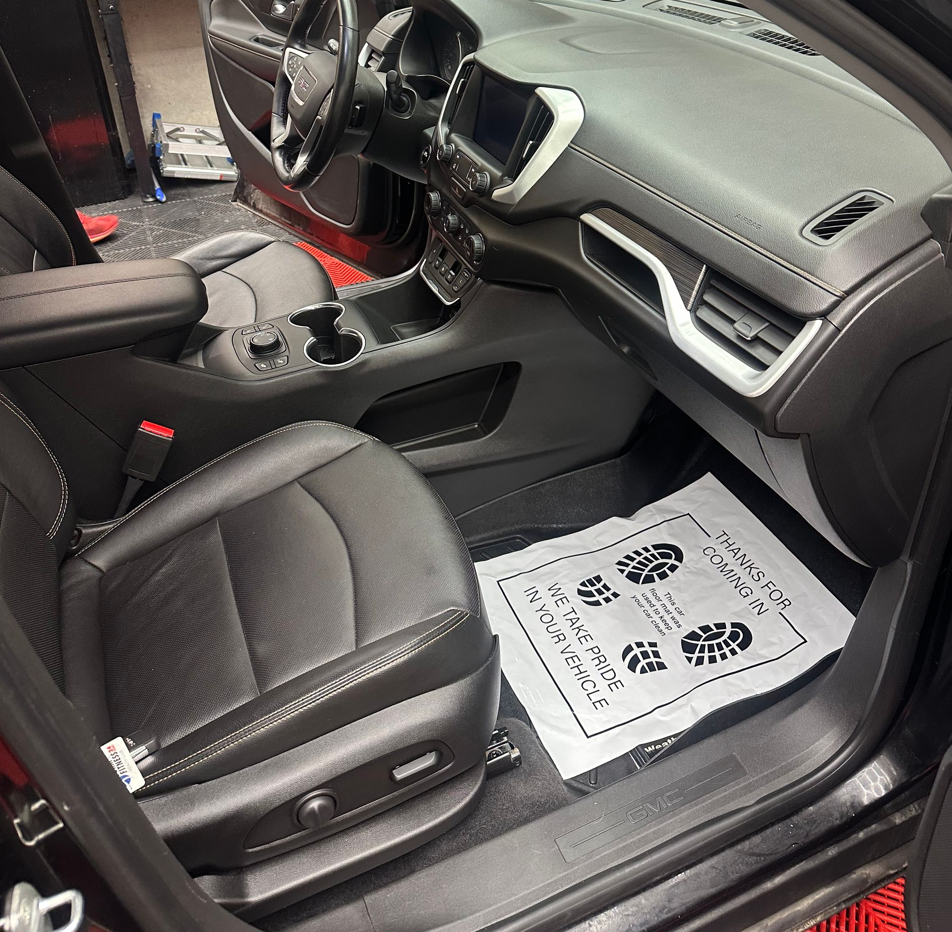 Car interior with black seats and dashboard, showing a floor mat with printed instructions on the passenger side