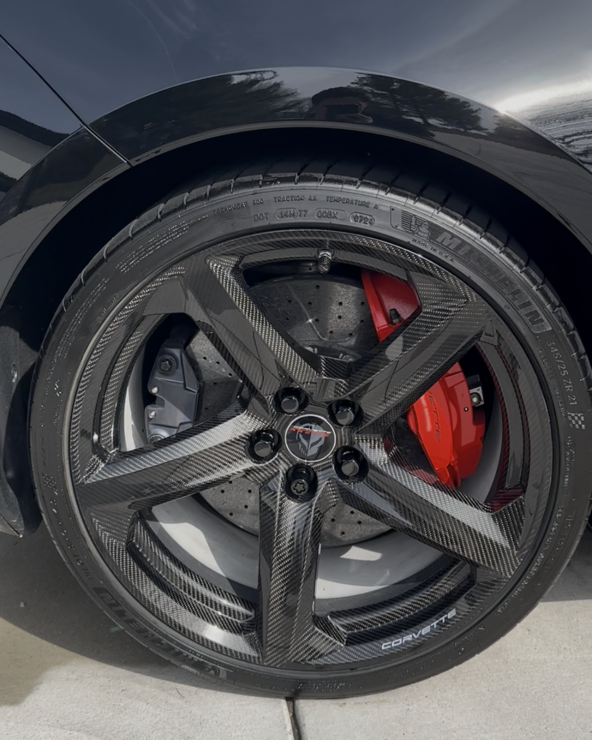 Black car wheel with glossy rim and red brake caliper on a driveway