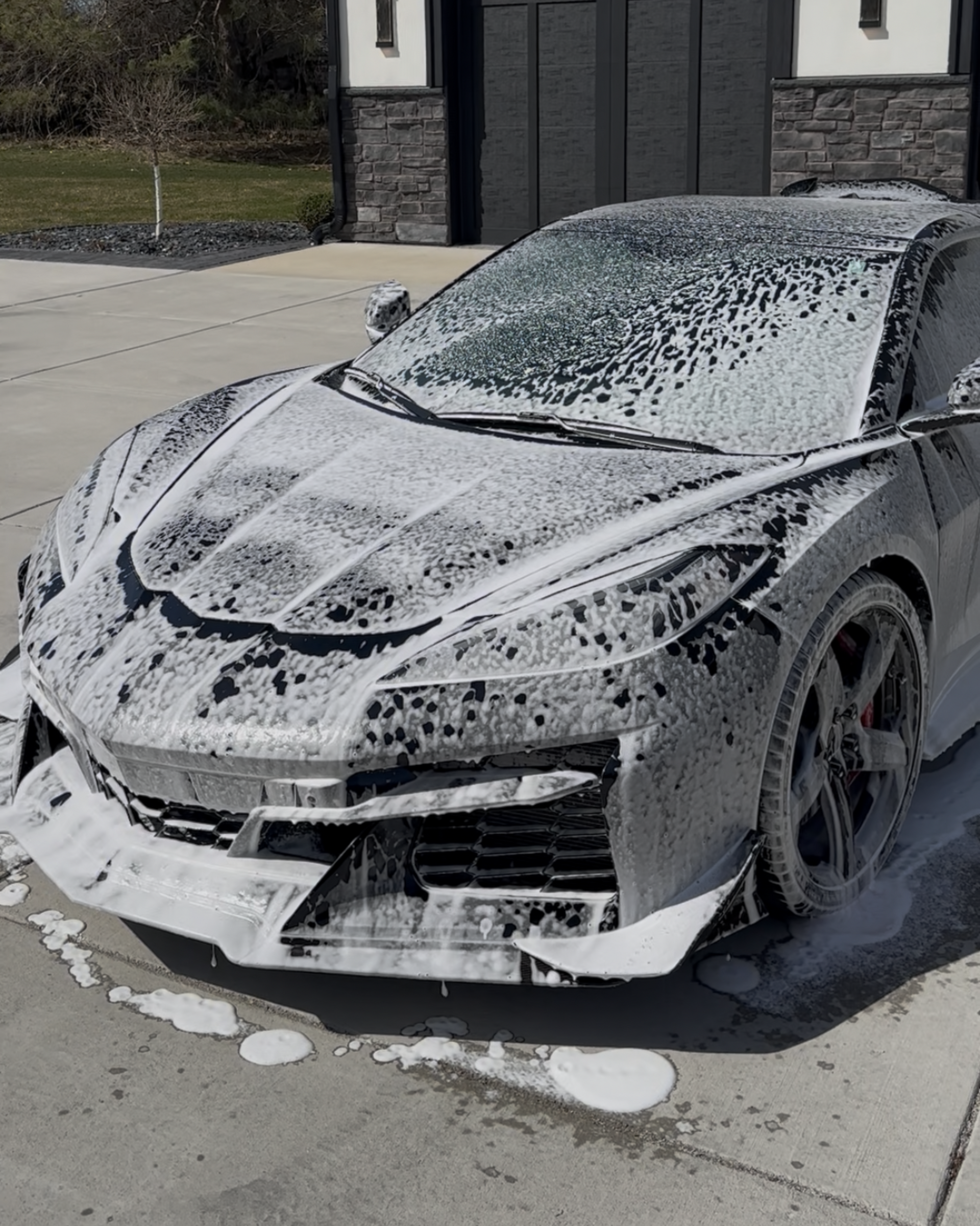 Snow-covered black sports car parked in front of a garage on a sunny driveway