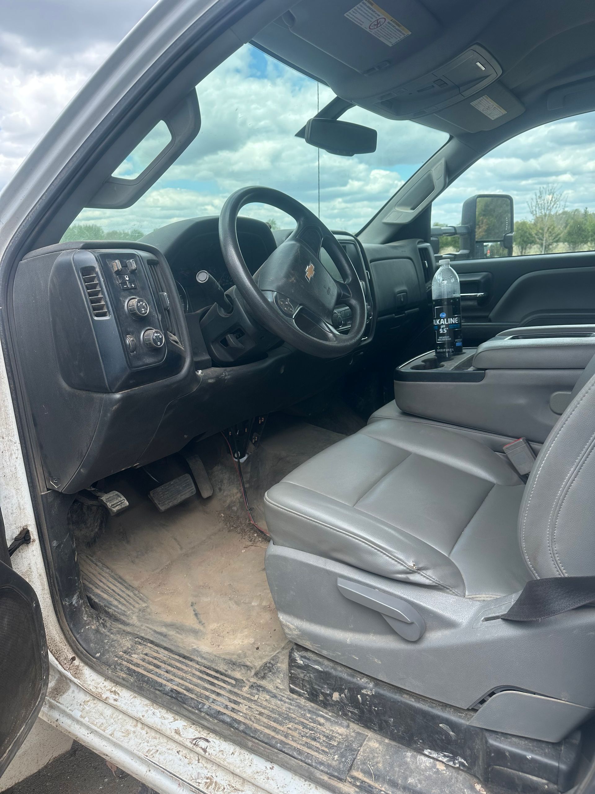 Car interior with a gray seat, steering wheel, and dashboard, viewed from the open red door.