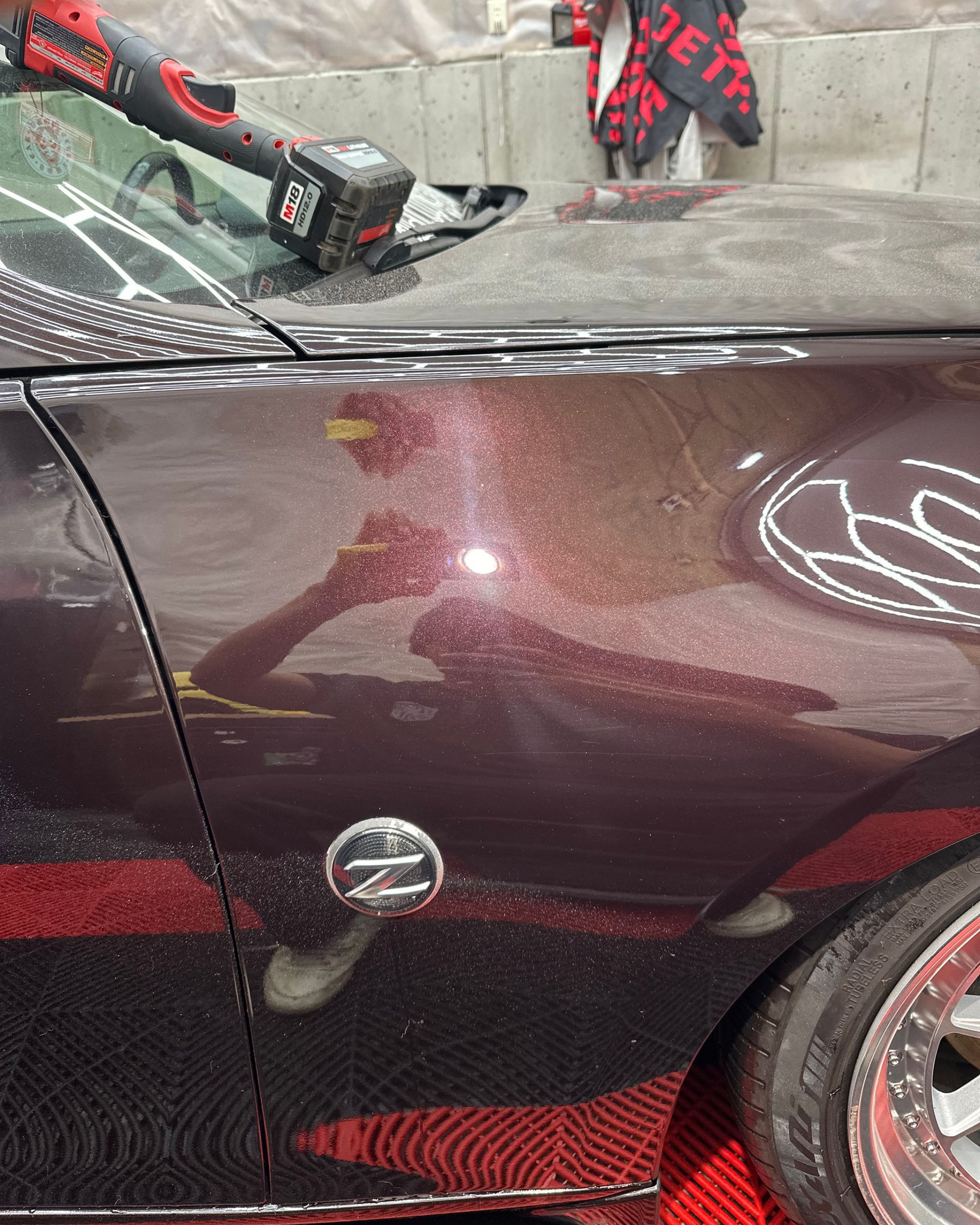 Close-up of a silver car’s rear quarter panel and bumper with a small red reflector.