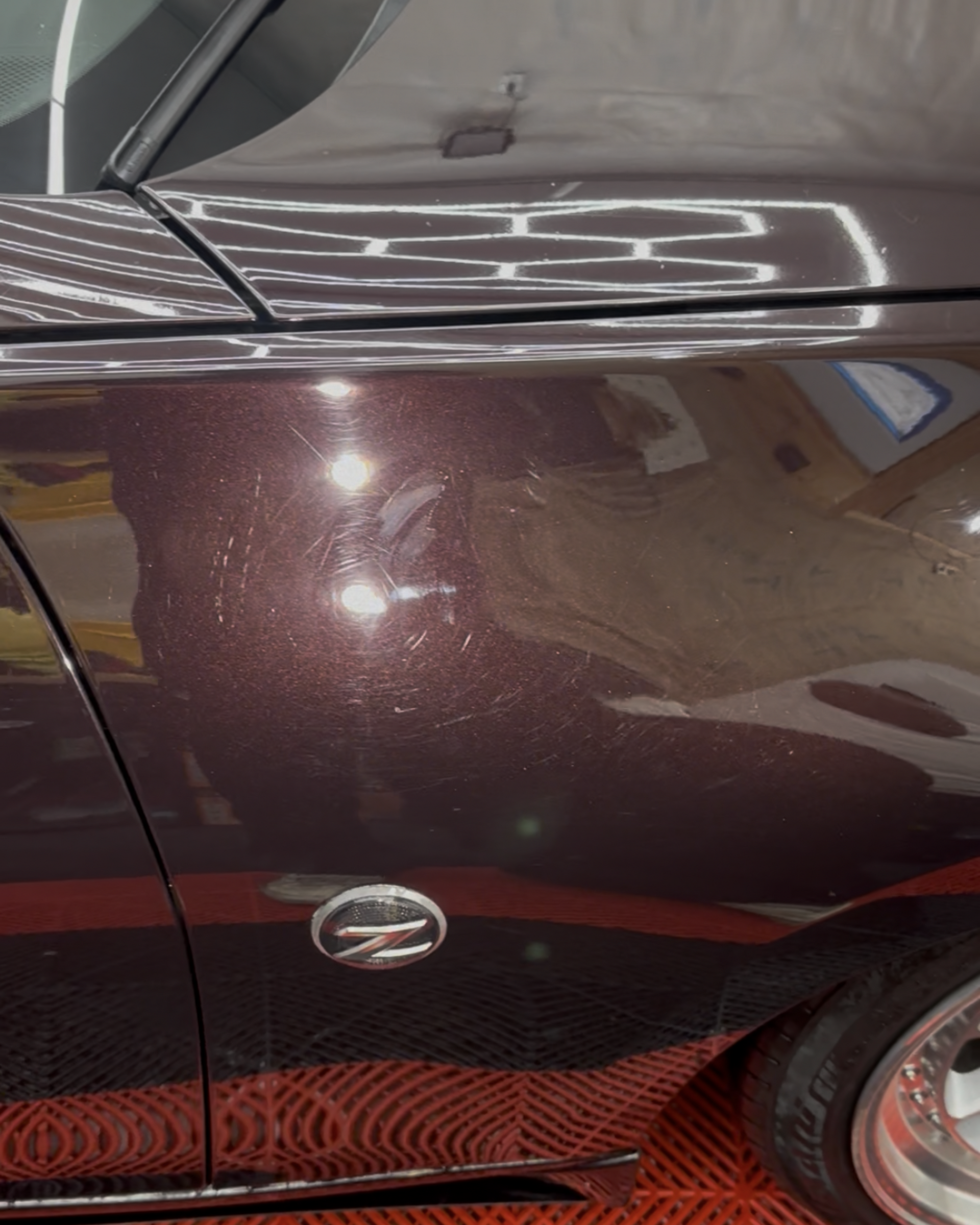 Maroon sports car under a silver car cover, with a black-and-red motorcycle helmet on the hood
