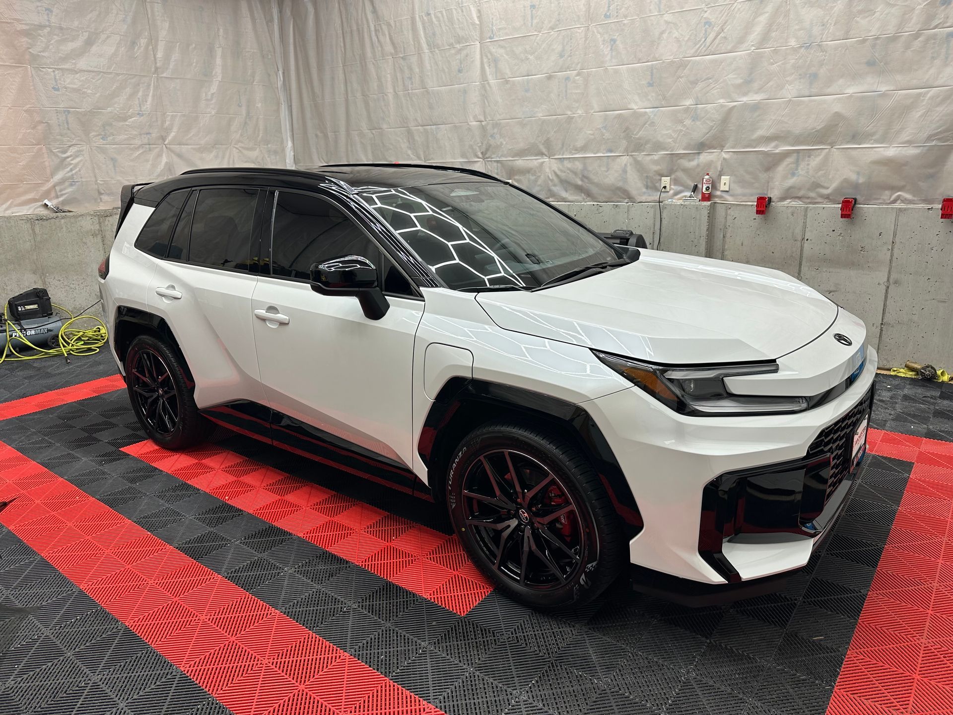 White SUV with black trim parked on a red-and-black checkered floor in a garage