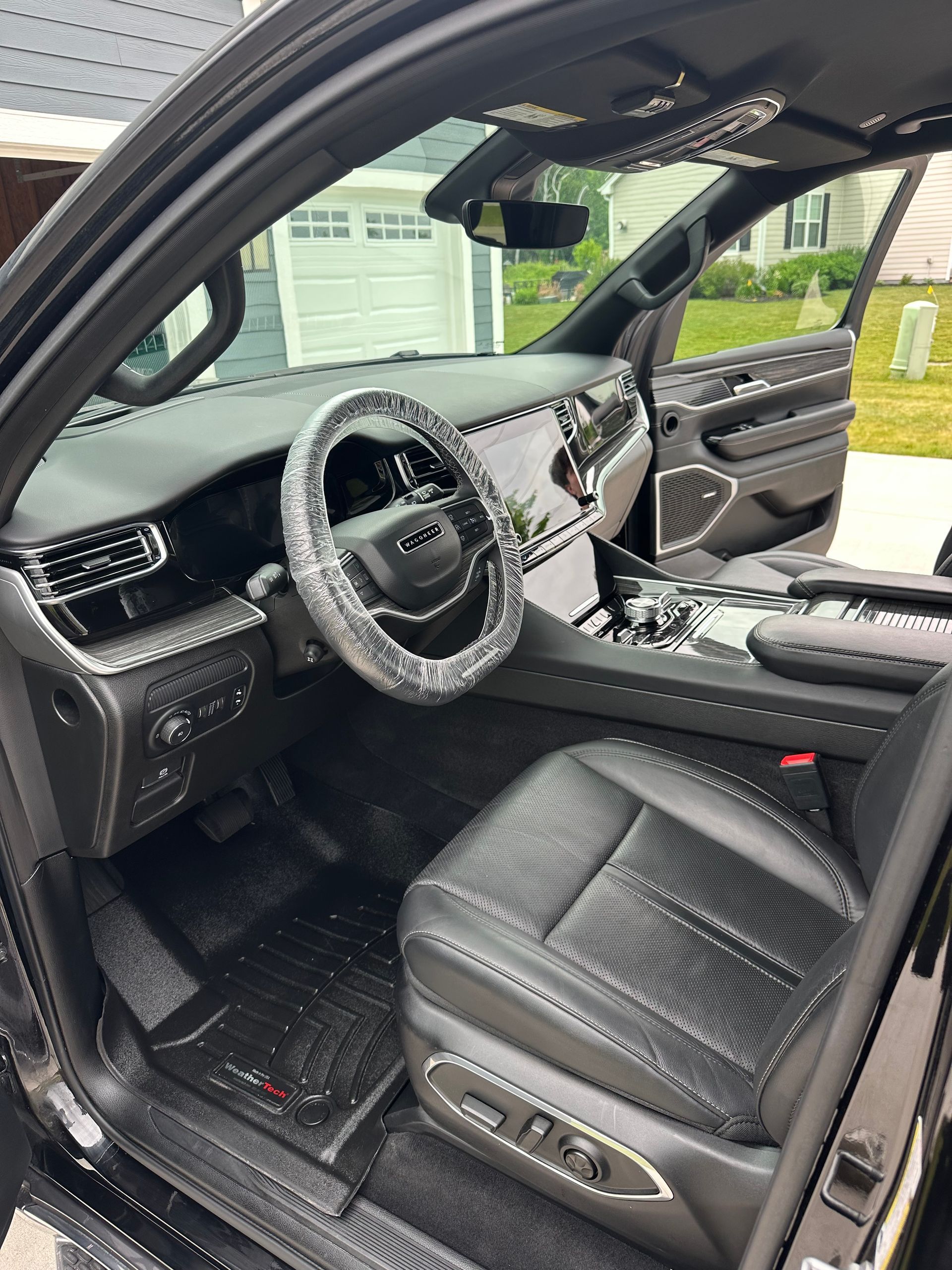 Blue car interior with black seats, steering wheel, and open driver’s door in a garage.