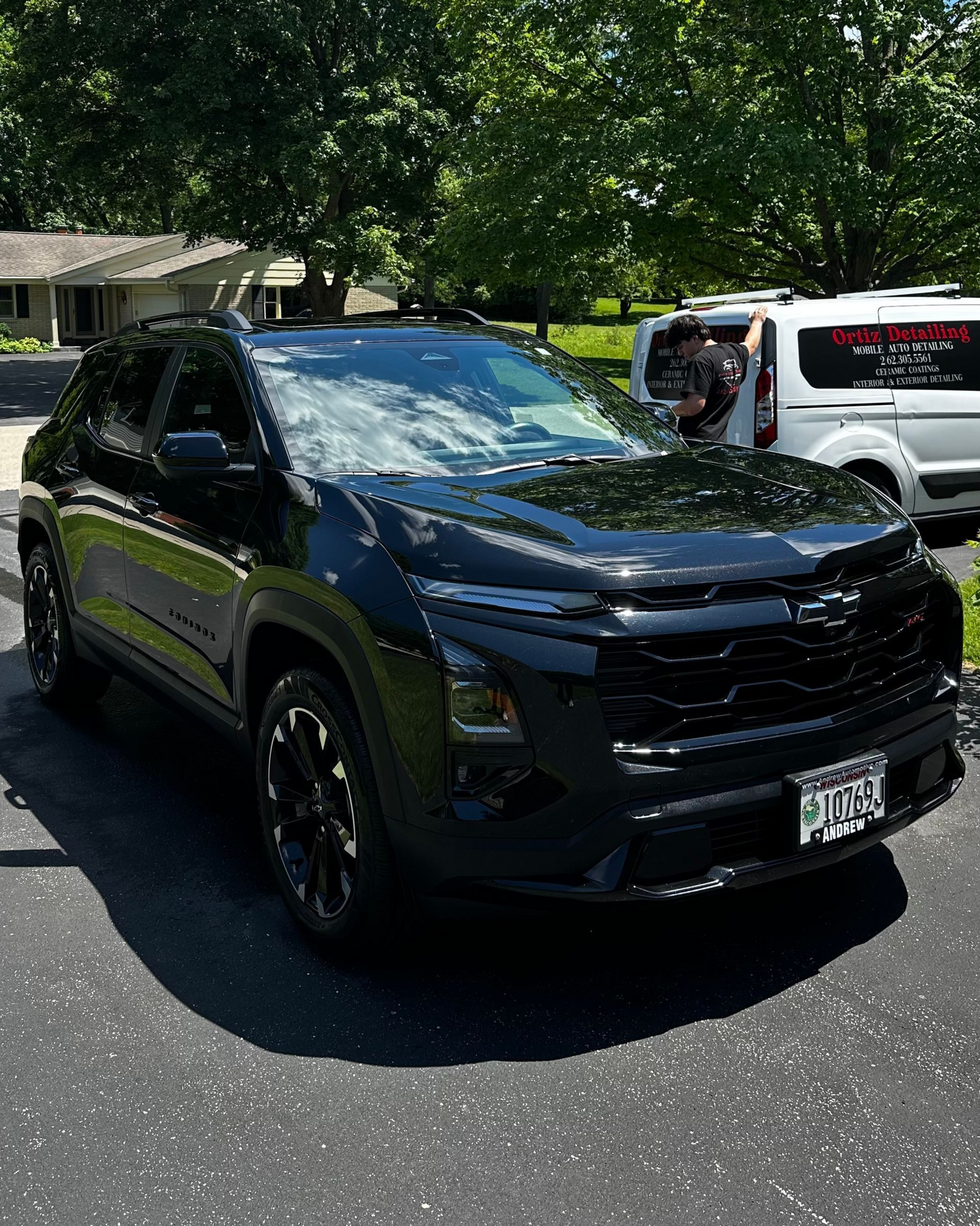 Black SUV parked in a sunny lot with trees and a white vehicle in the background.