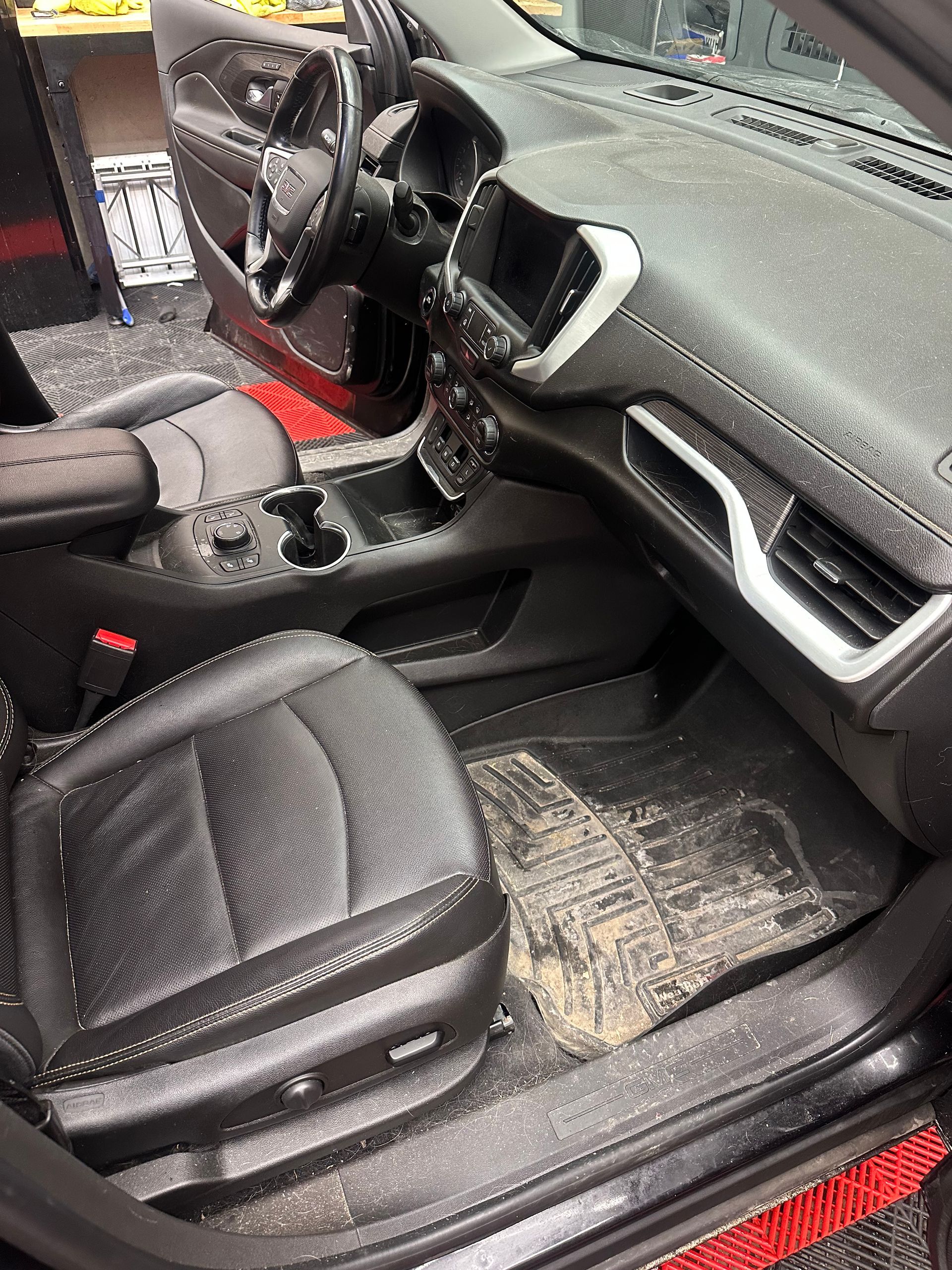 Car interior with black seats, red accents, and an open passenger door, showing the front cabin and floor mats