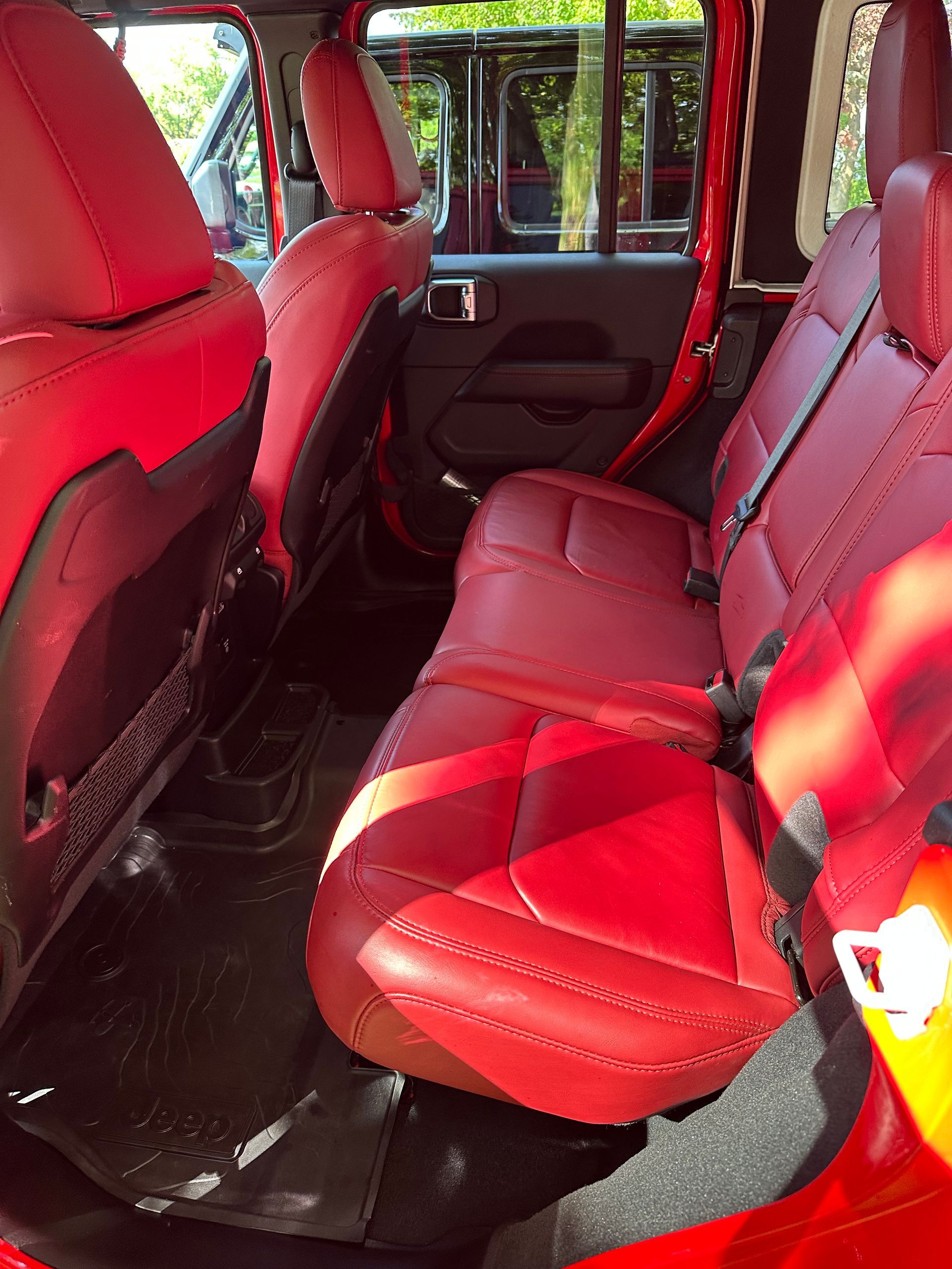 Red leather back seat inside a vehicle, with a dark interior and sunlight streaming in.