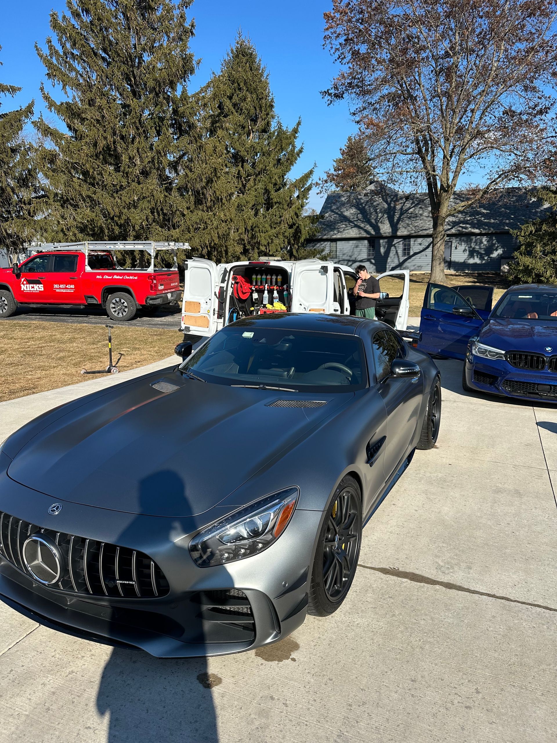 Gray Mercedes convertible parked in a driveway, with people and other cars in the background