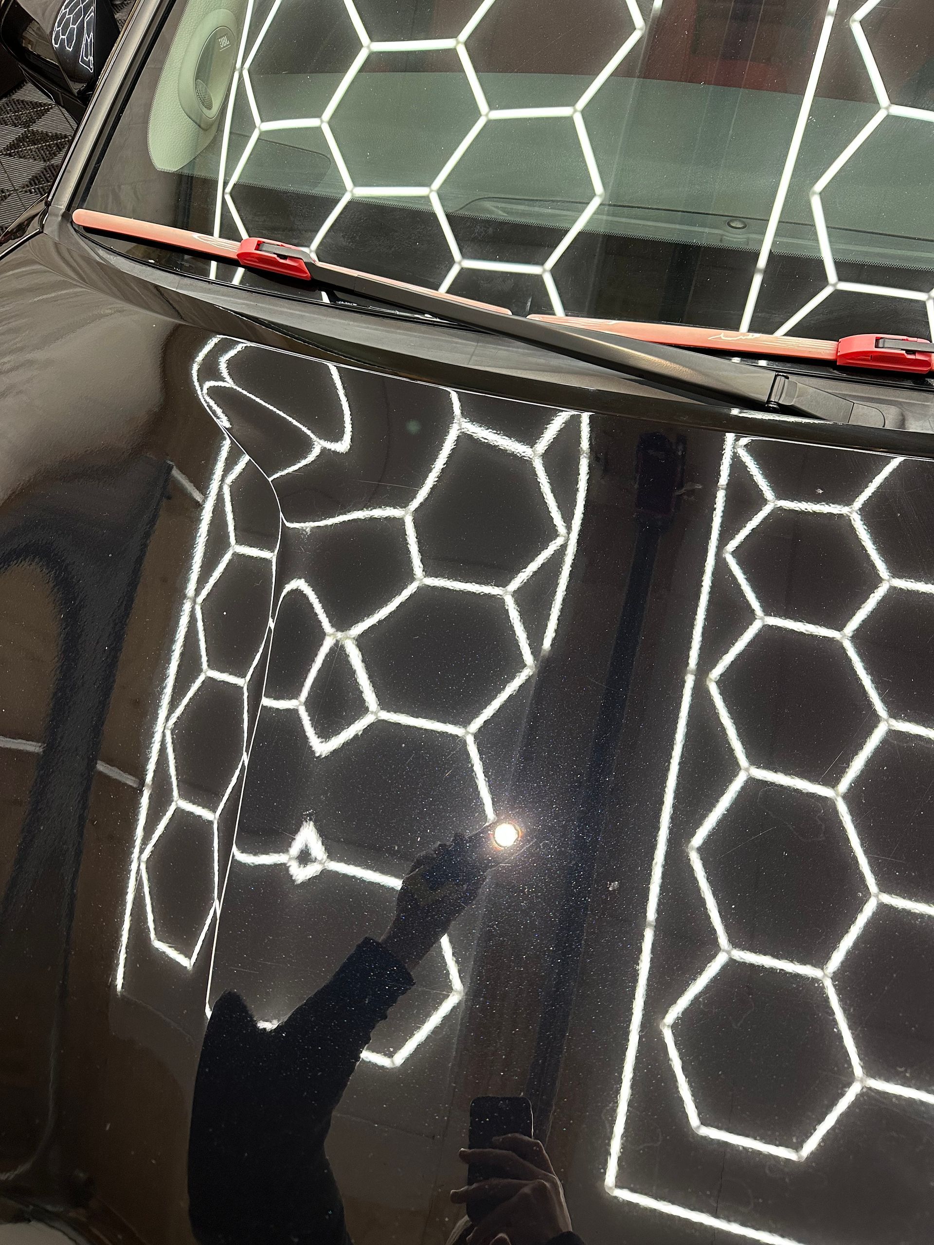 Black car hood reflecting bright hexagonal lights, with a red stripe near the windshield.