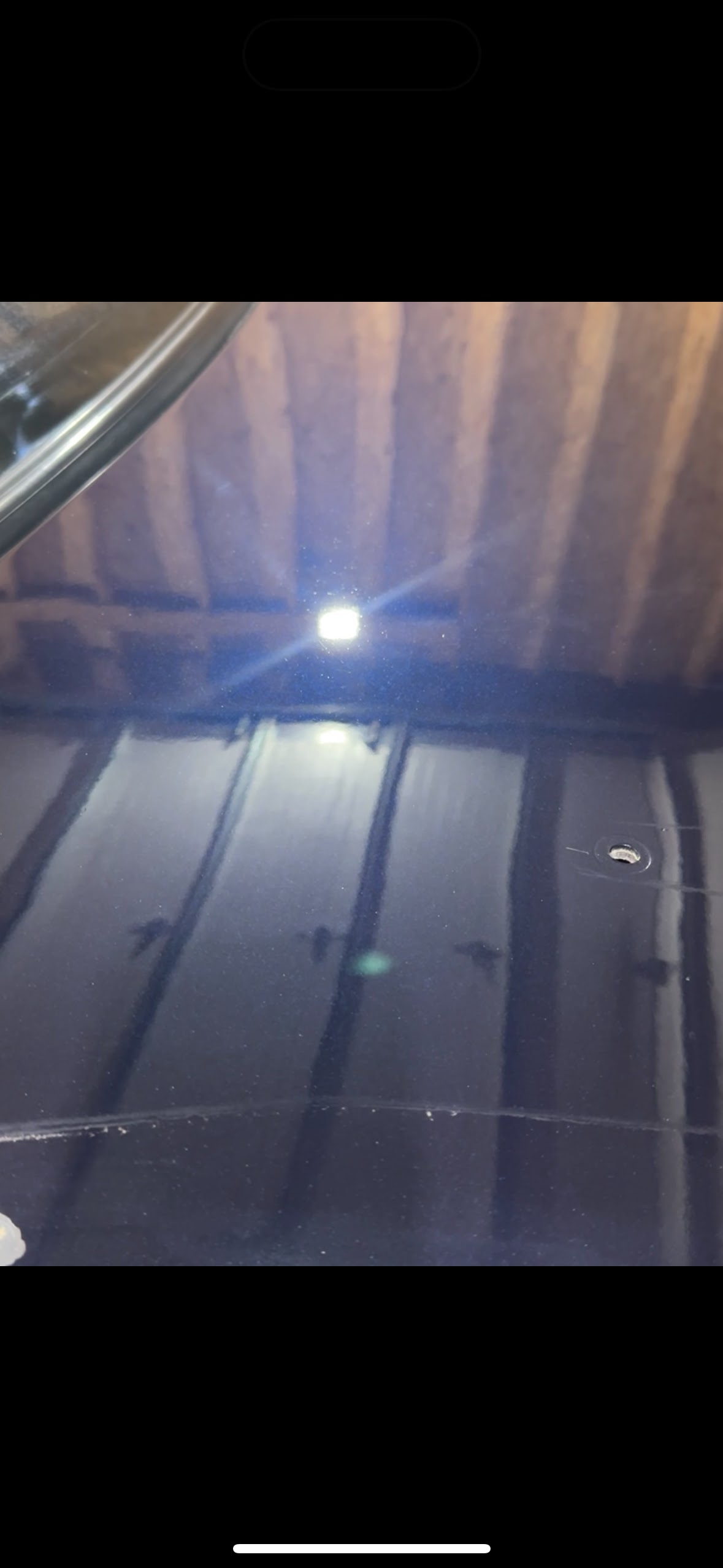 Dimly lit car interior with a bright ceiling light reflecting on a dark window or sunroof.
