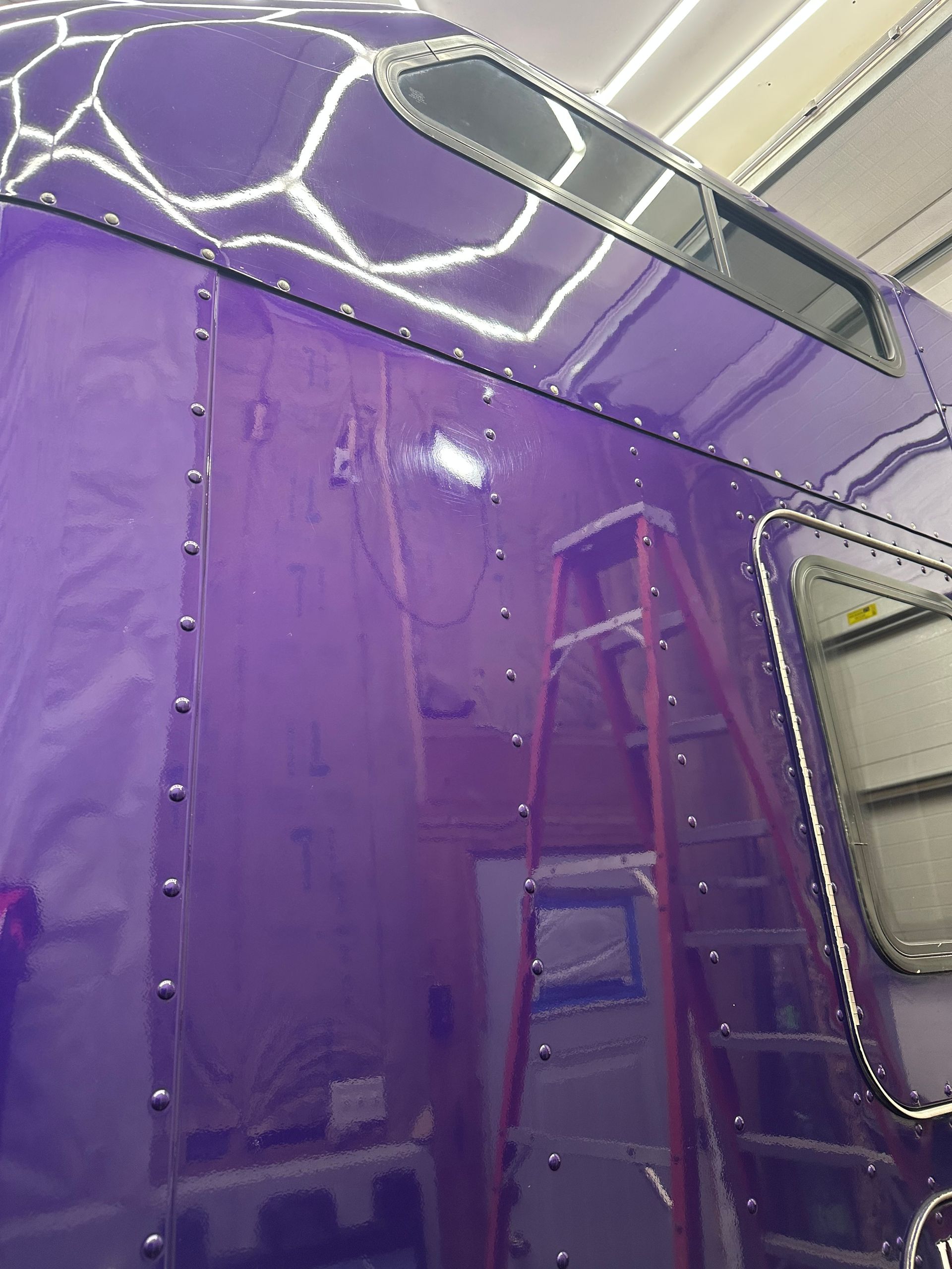 Purple vehicle side panel with ladder and window, viewed close up.