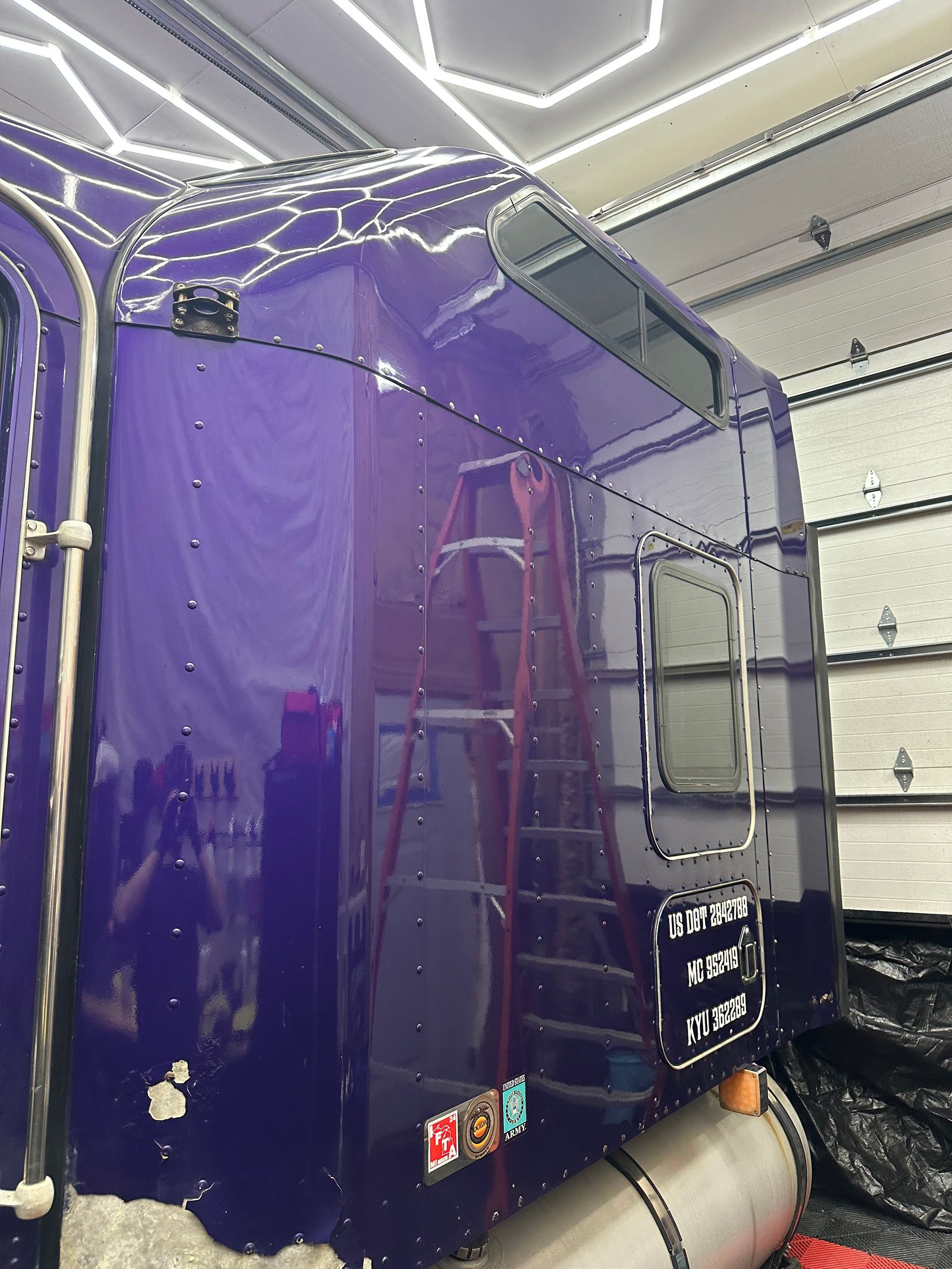 Purple semi-truck cab inside a garage, with a ladder and chrome fuel tank visible.