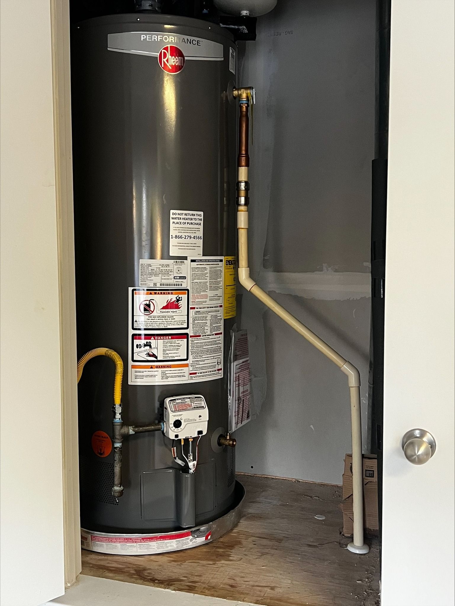 Water heater in a small closet, with pipes. Ground is wet.