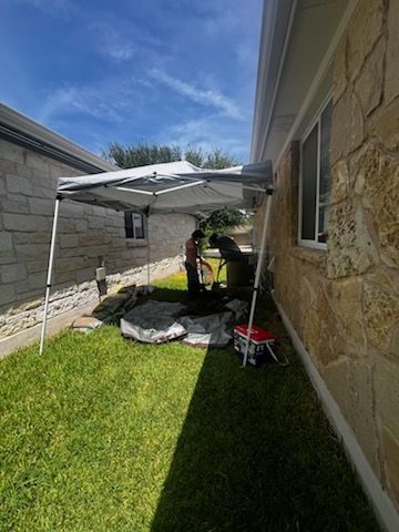 People under a canopy working in a grassy yard next to a stone house on a sunny day.