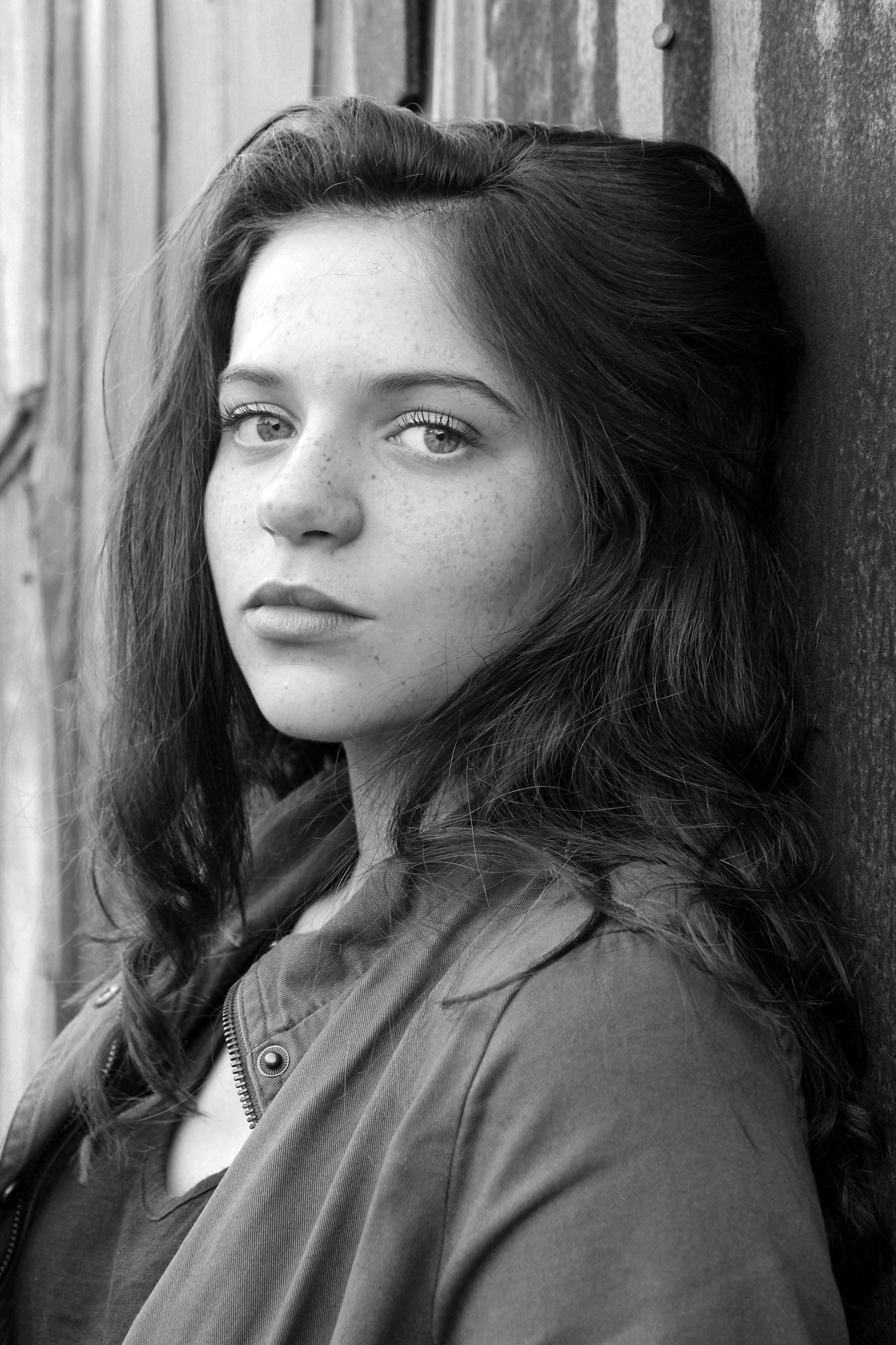 A black and white photo of a woman leaning against a wall.