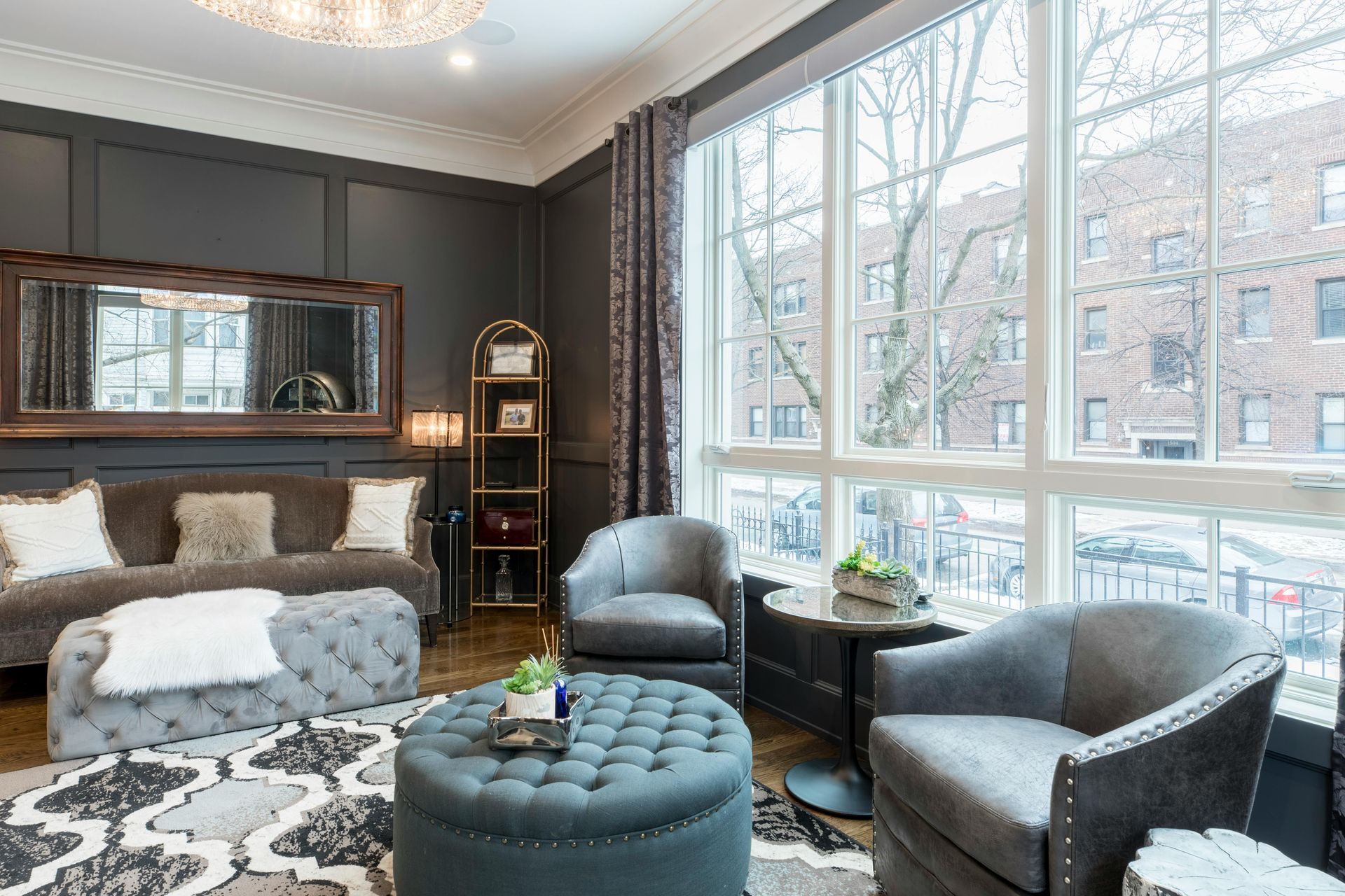 A living room with a couch , chairs , ottoman and large windows.