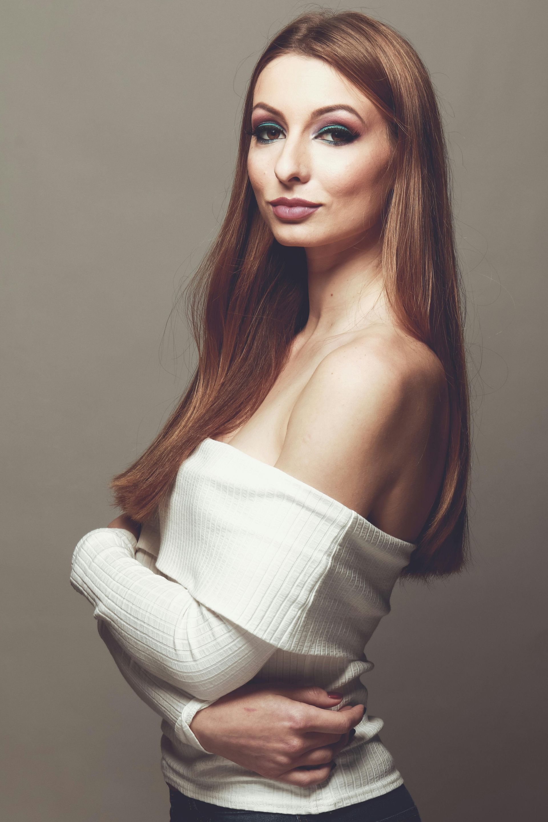 A woman with long hair is wearing a white off the shoulder sweater.