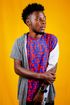 A young man wearing a colorful shirt and a watch is standing in front of a yellow background.