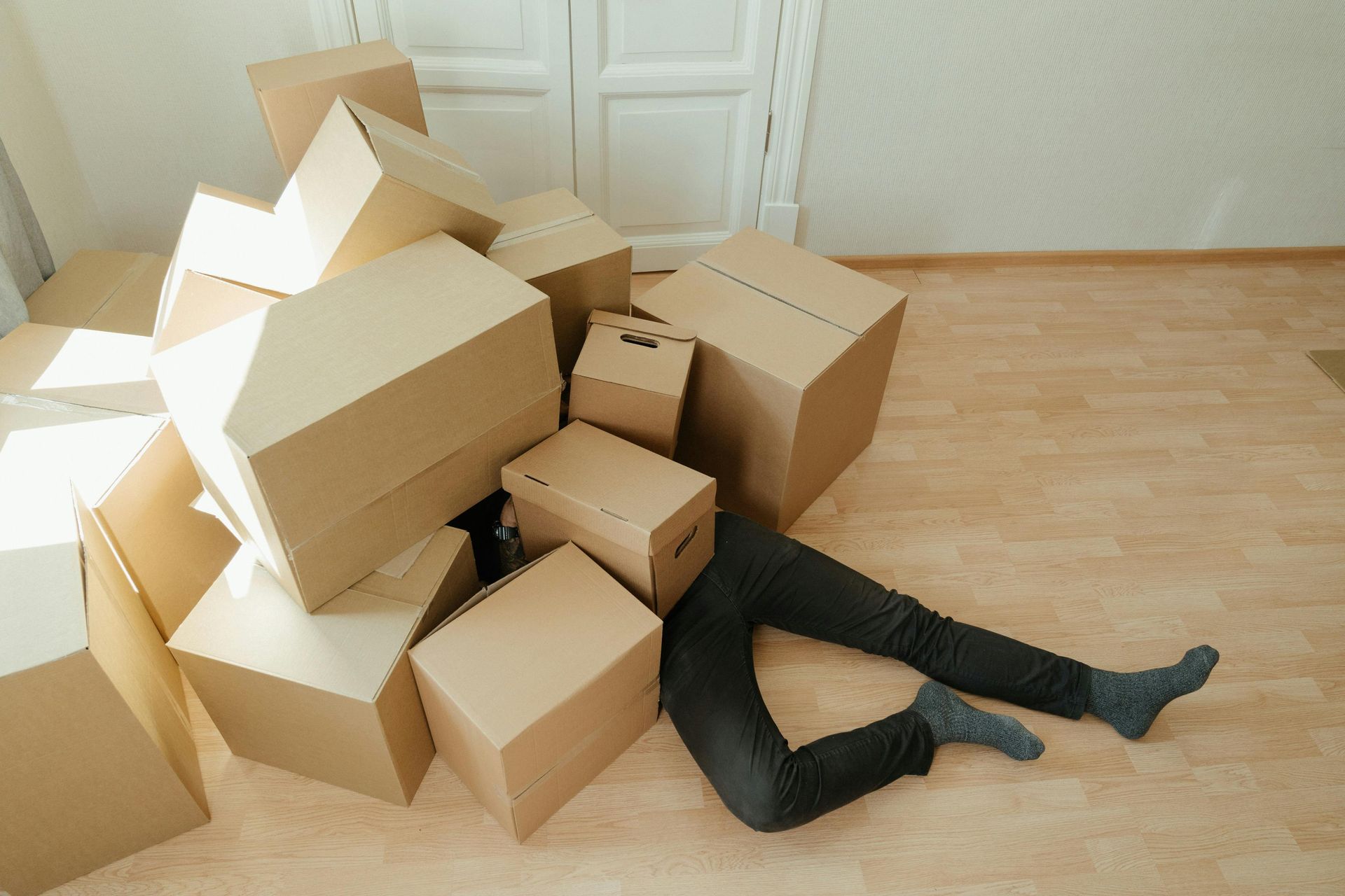 A person is laying on the floor surrounded by cardboard boxes.