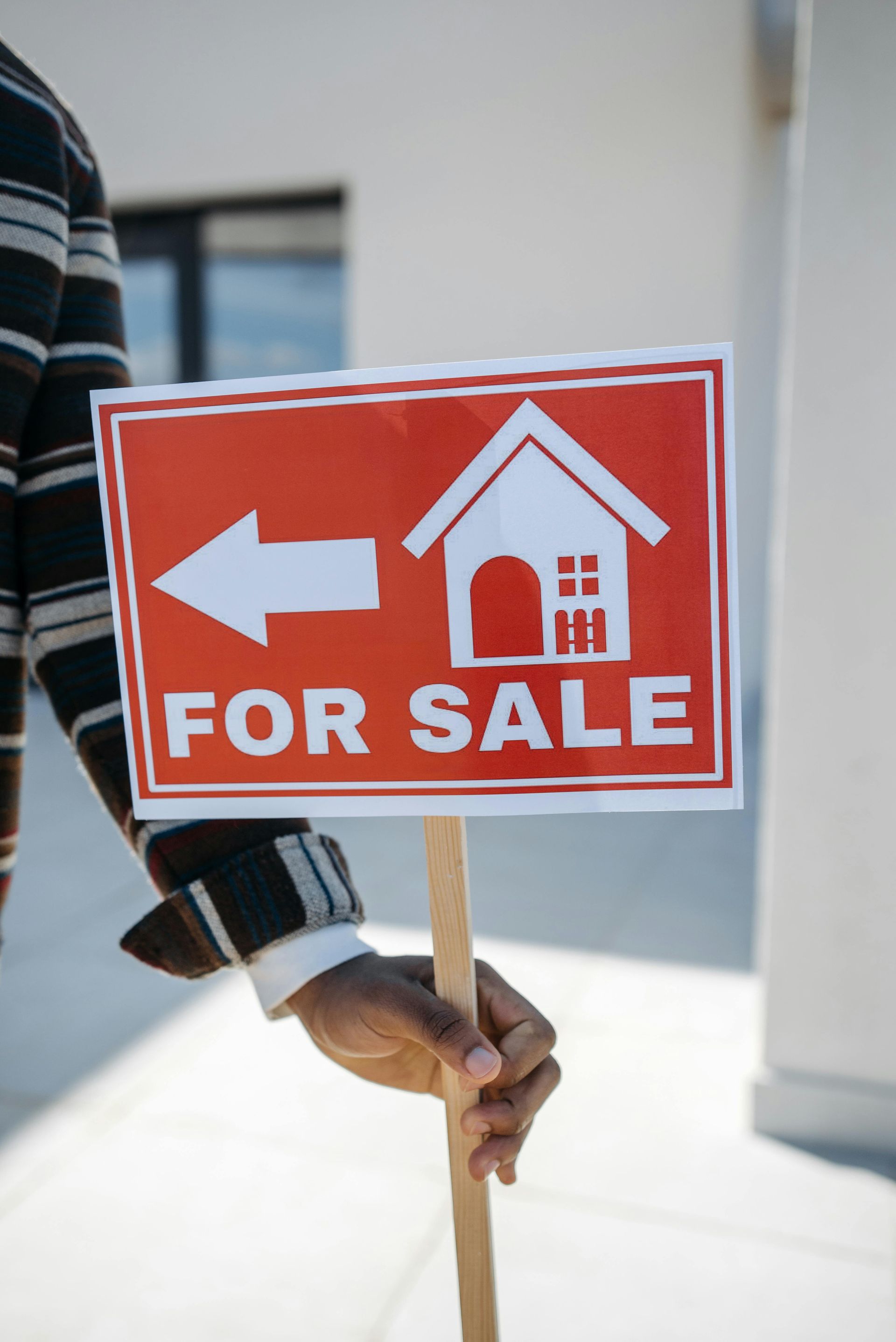 A person is holding a for sale sign in front of a house.