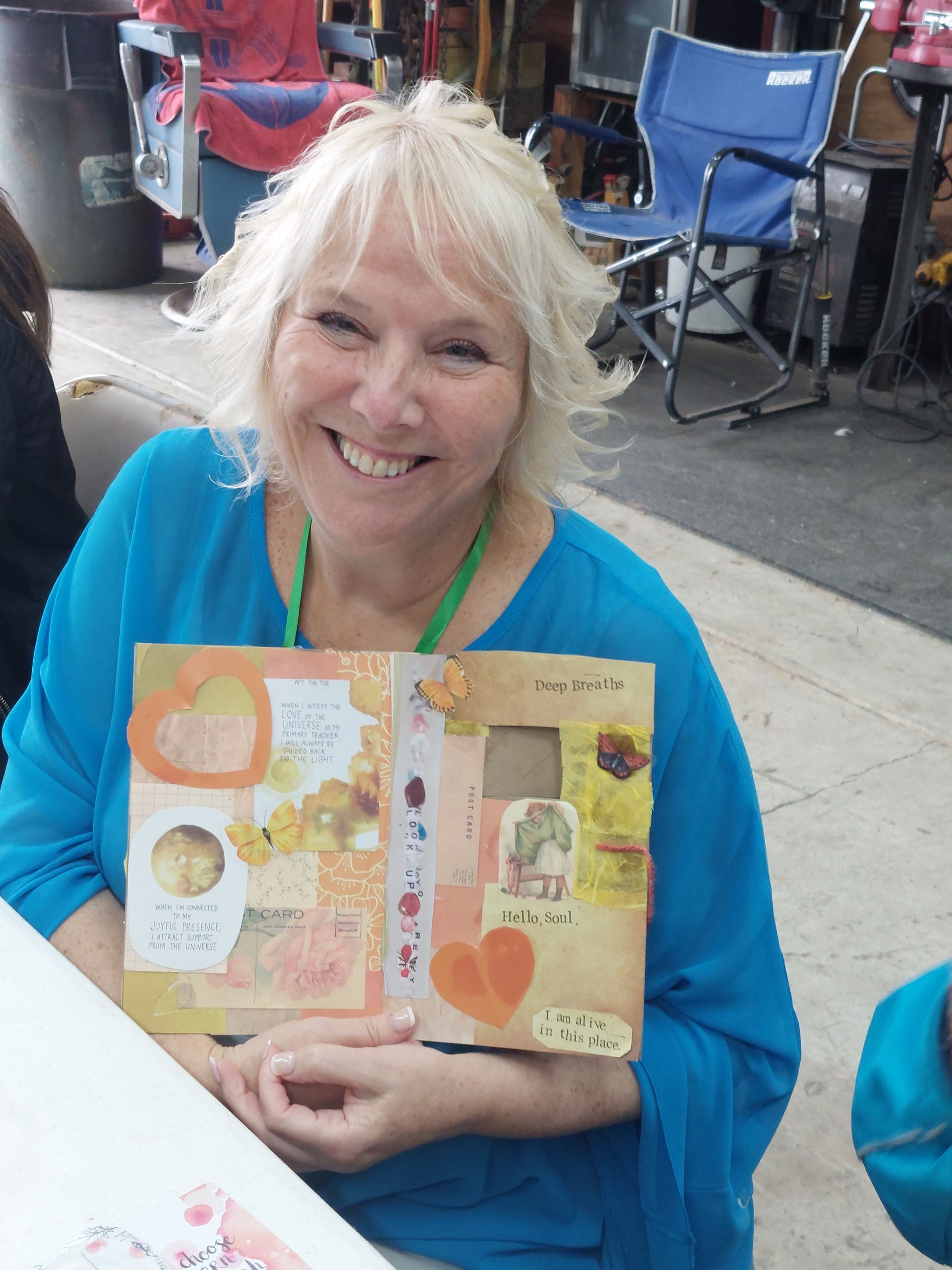 A woman in a blue shirt is smiling and holding a book
