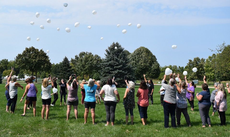 A group of people are standing in a field throwing balloons in the air.